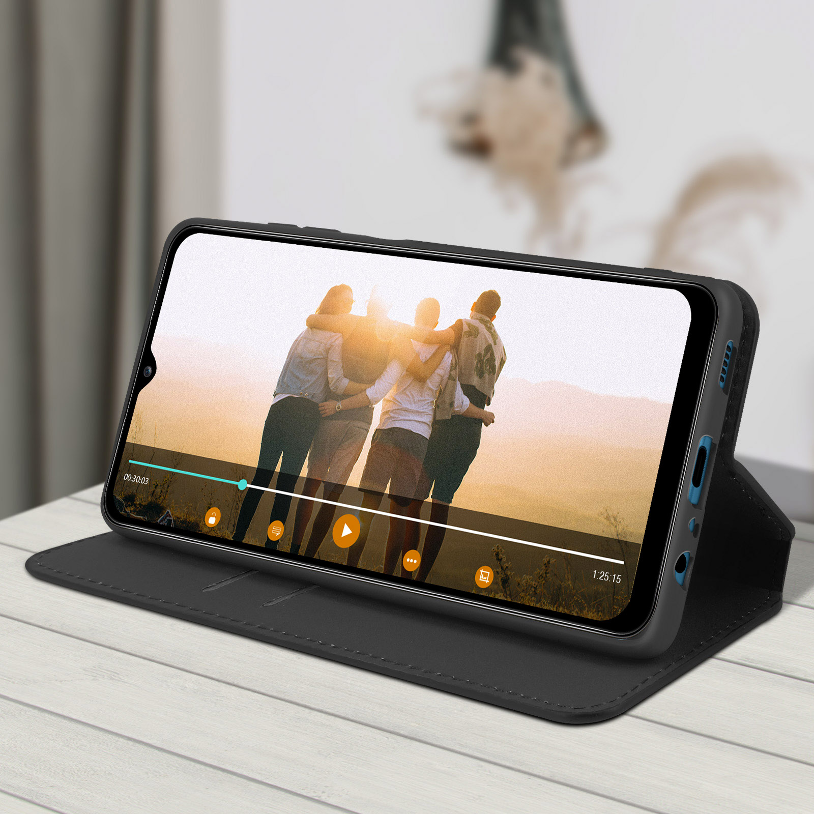 Téléphone dans un étui noir, affichant une vidéo. L'étui est ouvert et posé sur une table en bois blanche.