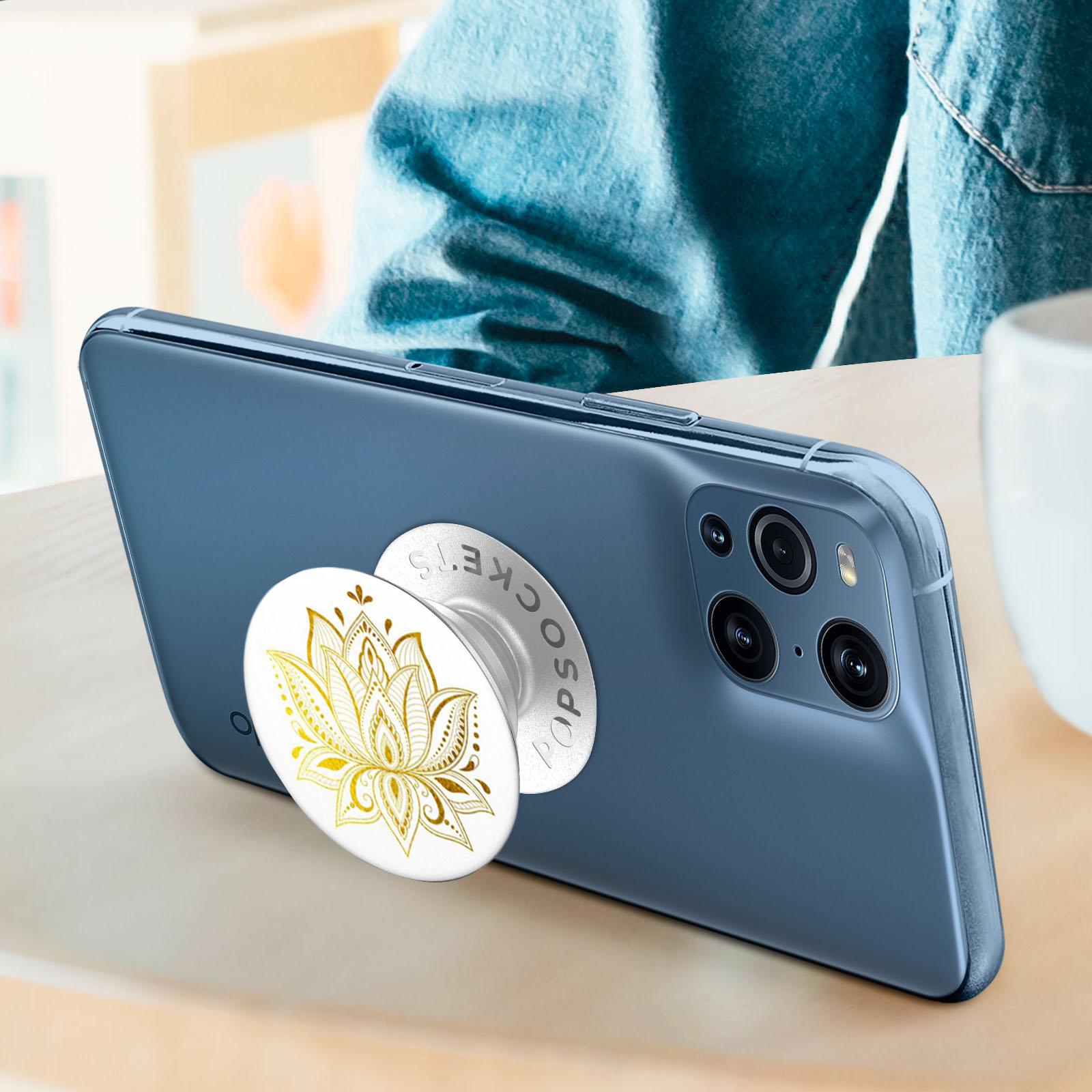 Blaues Telefon mit goldenem PopSocket-Design. Das Telefon liegt auf einer Holzoberfläche.