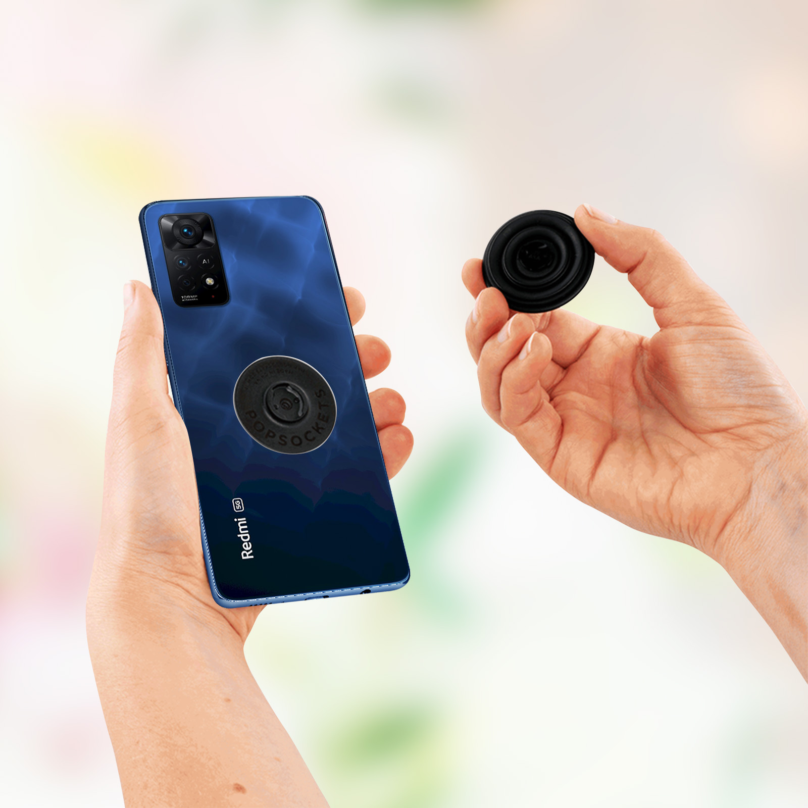 Hände halten ein Telefon mit blauer Hülle und einen PopSocket. Verschwommener Hintergrund.