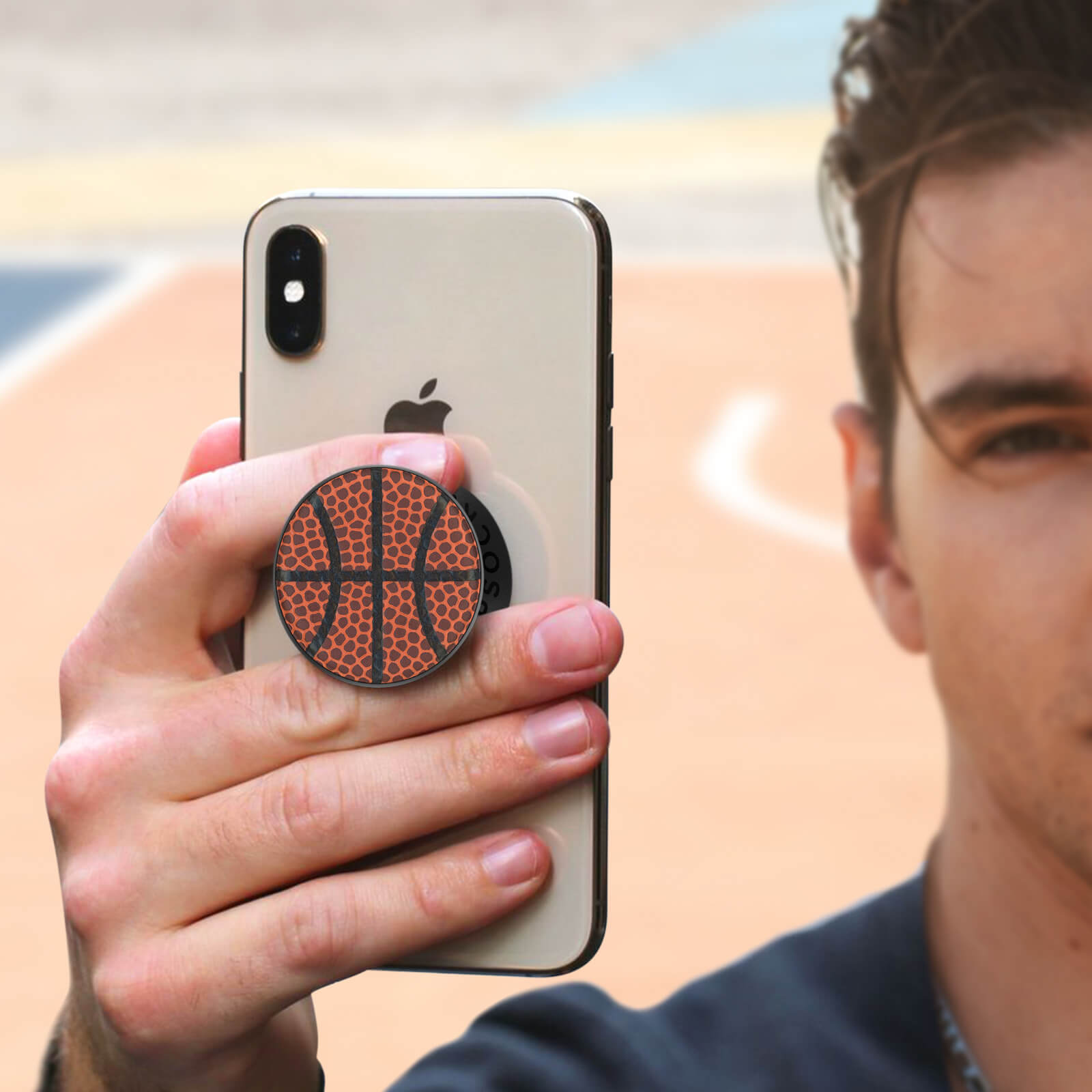 Eine Person hält ein Telefon mit einem Popsocket im Basketball-Design vor einem Basketballfeld.