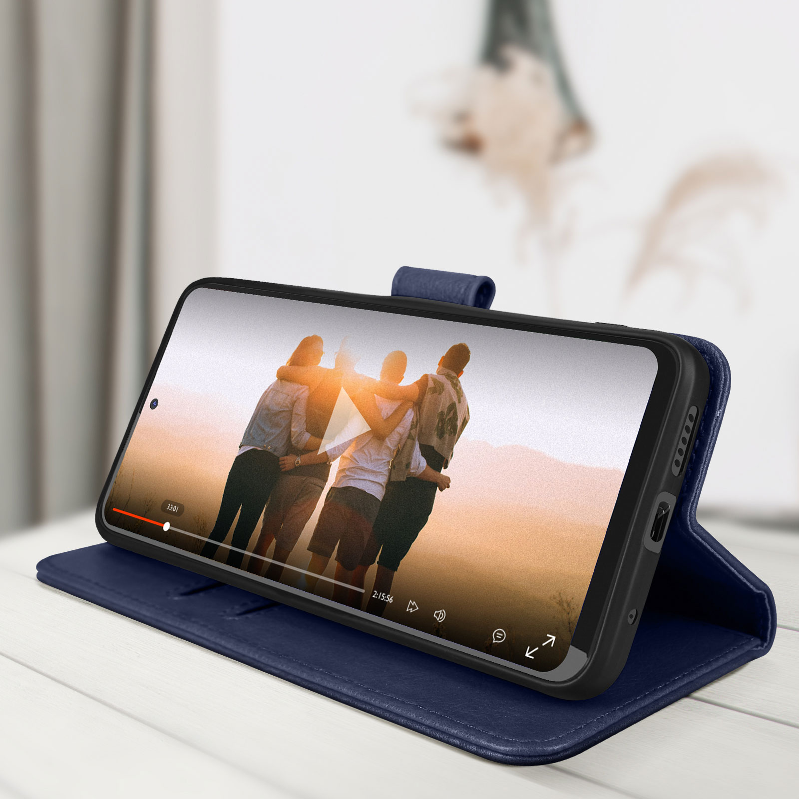 Telefono in una custodia blu, che riproduce un video, appoggiato su un tavolo bianco. Sfondo sfocato.