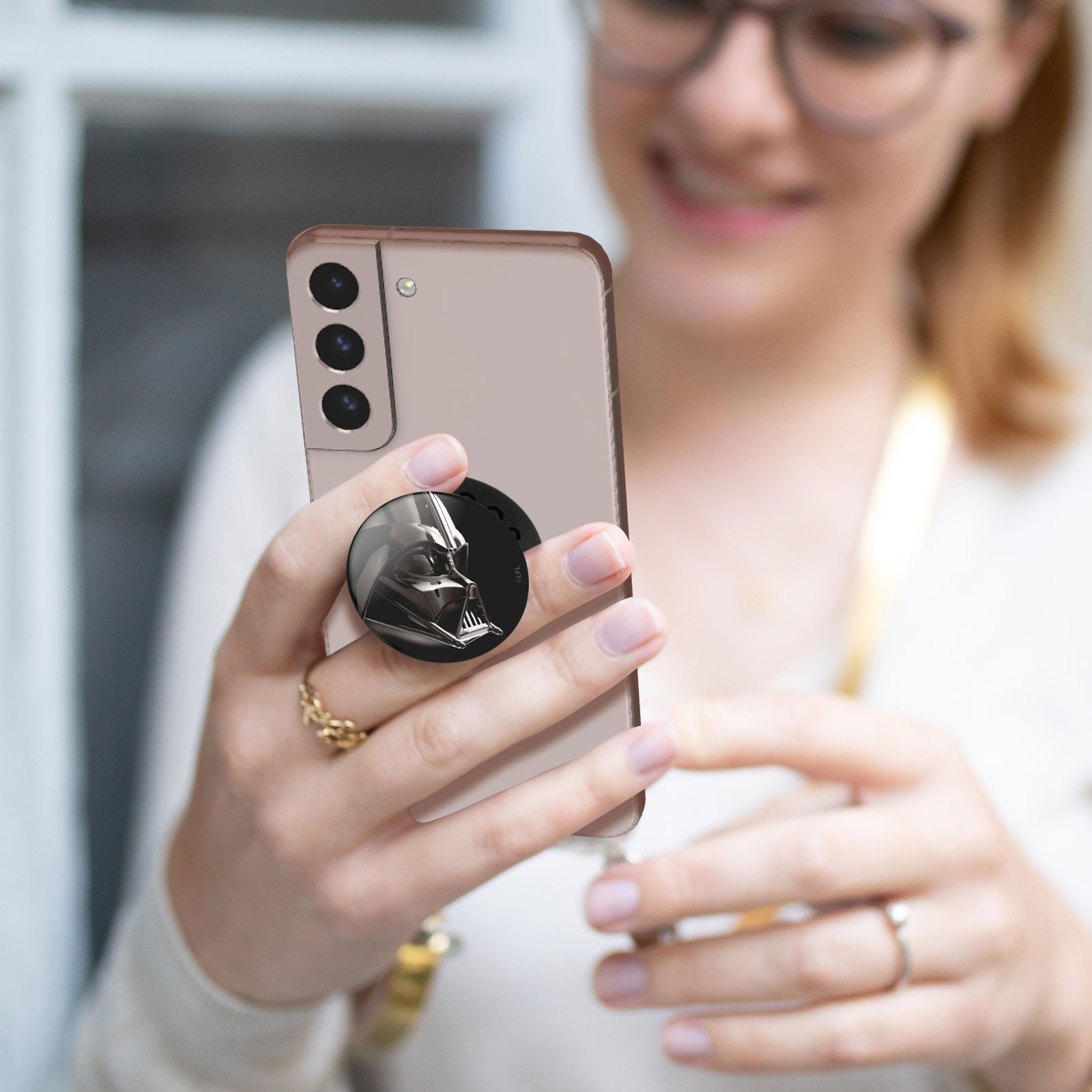 Eine Frau hält ein Telefon mit einem Darth-Vader-Pop-Socket. Sie trägt eine Brille.