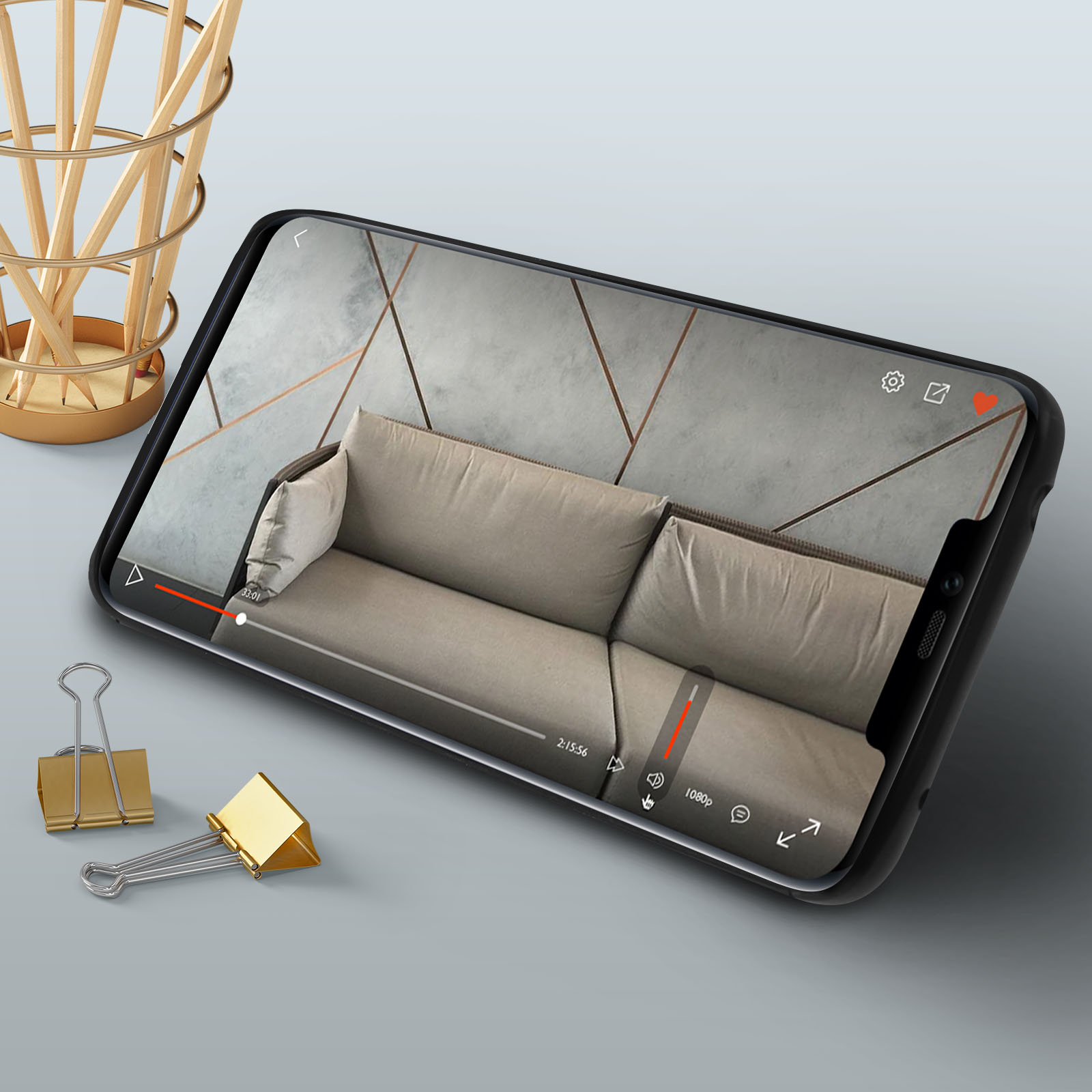 Telefono che mostra un video. Il telefono è su una superficie con forniture per ufficio. Sfondo grigio chiaro.