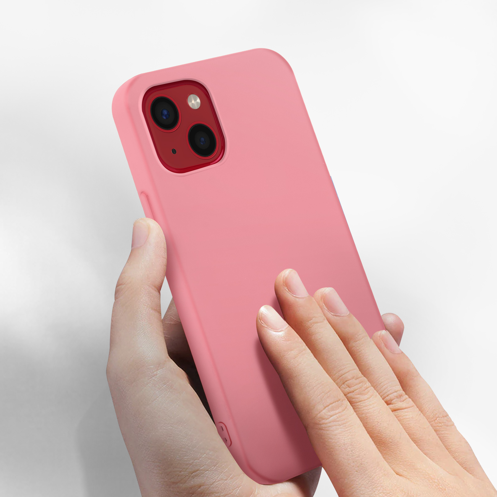 Un téléphone rose est tenu par une main. Le téléphone a un module de caméra rouge. Le fond est blanc.