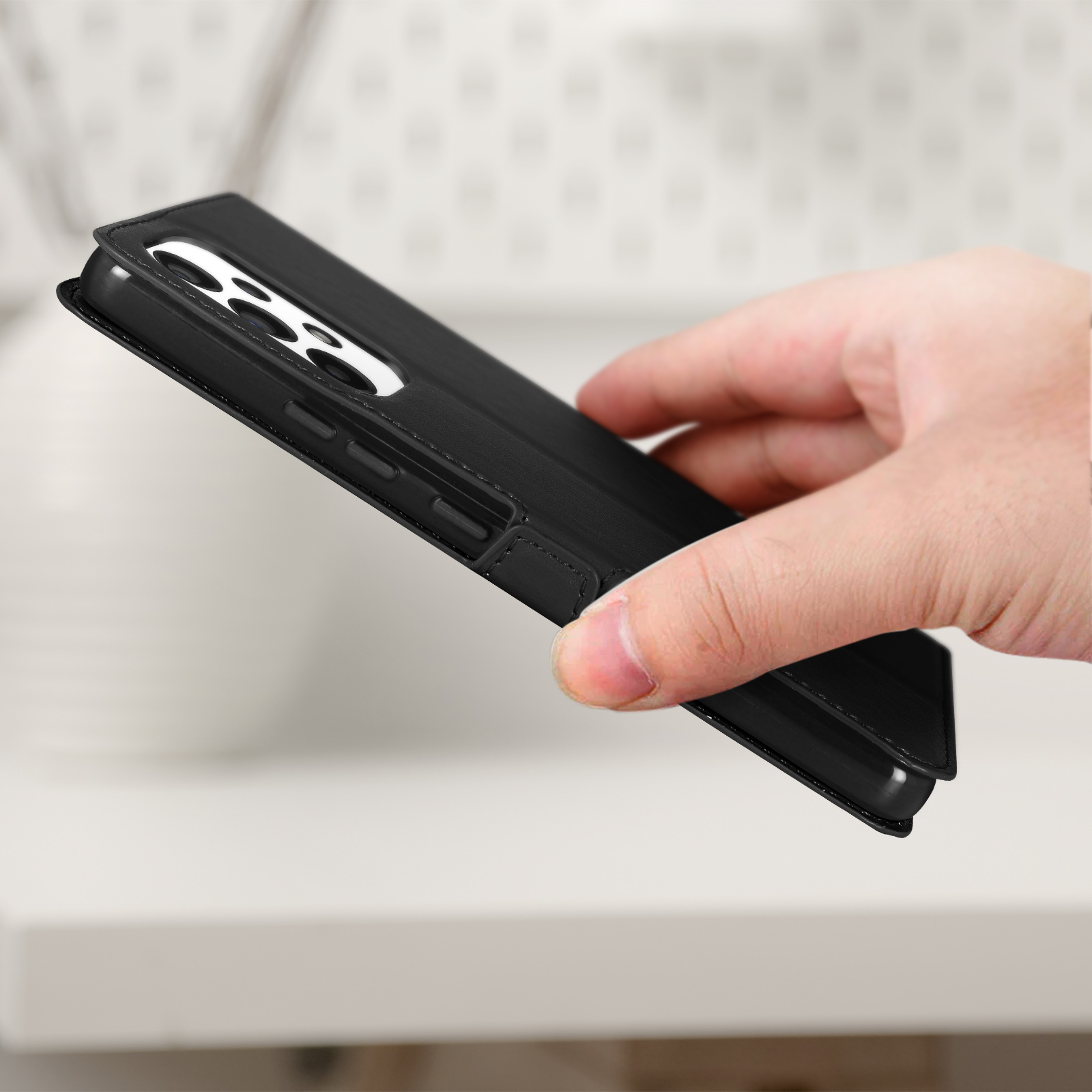 Une coque de téléphone noire est tenue. L'étui est sur une surface blanche. Le téléphone est fermé.