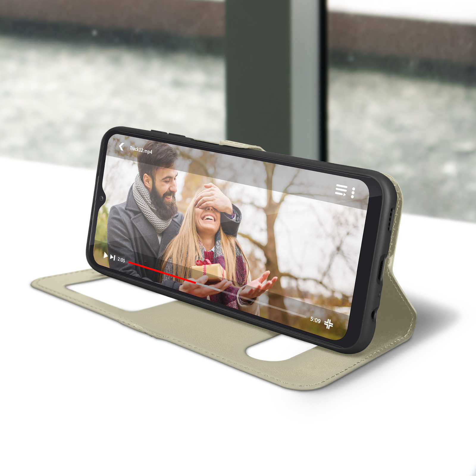 Le téléphone affiche un couple regardant une vidéo. Le téléphone est dans un étui beige. L'arrière-plan est flou.