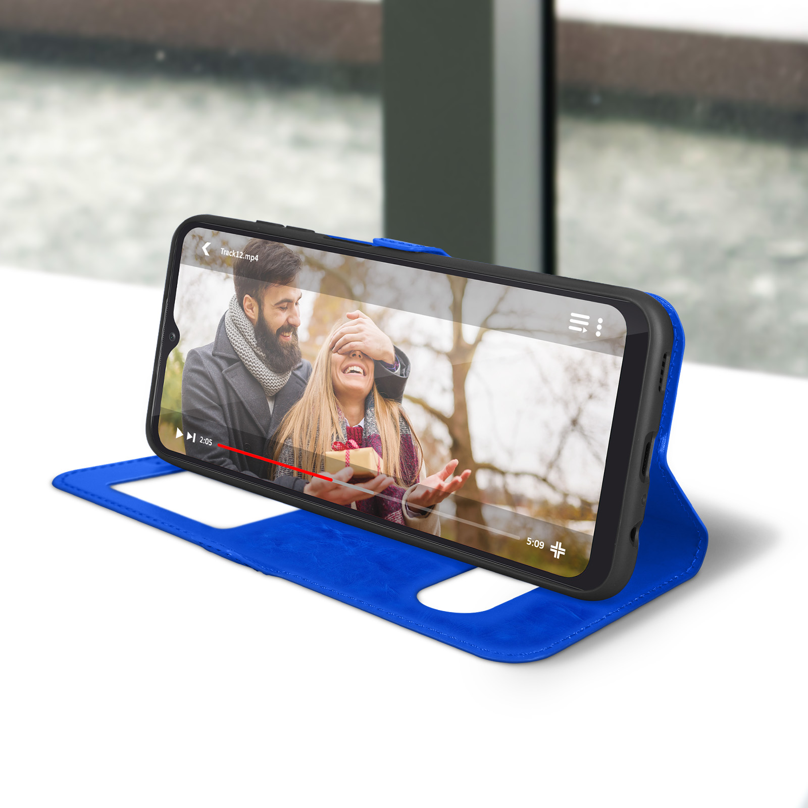 Téléphone avec vidéo à l'écran. Étui bleu ouvert. Couple dans la vidéo. Table blanche, fond de fenêtre.
