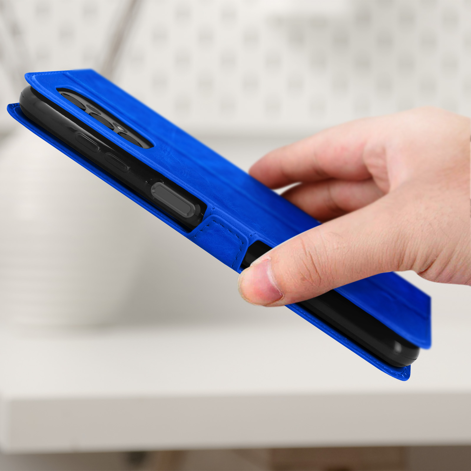 Une main tenant un étui de téléphone bleu, partiellement ouvert, montrant le téléphone à l'intérieur.
