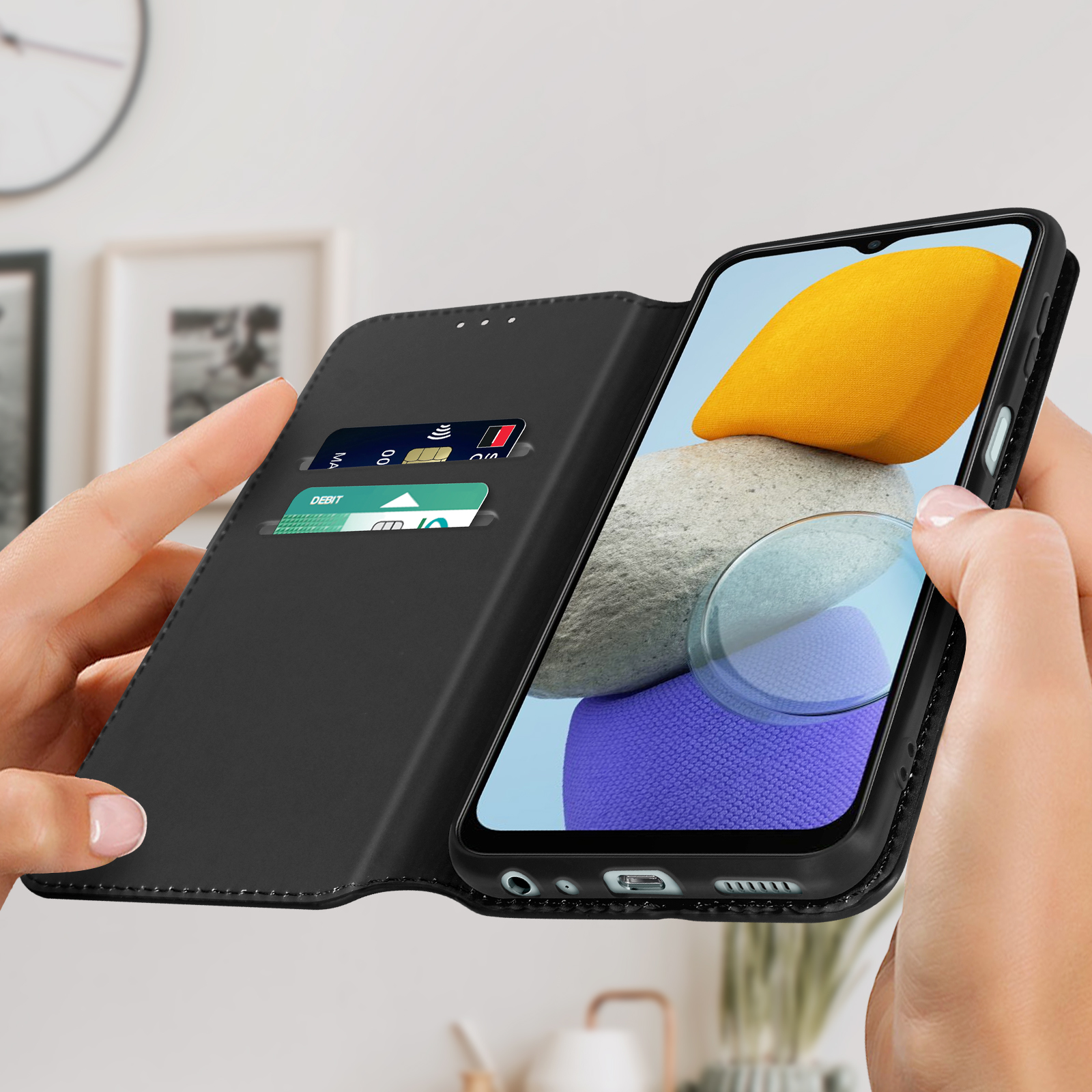 Mani che tengono un telefono nero in una custodia a portafoglio nera. Le carte di credito sono visibili nel portafoglio.
