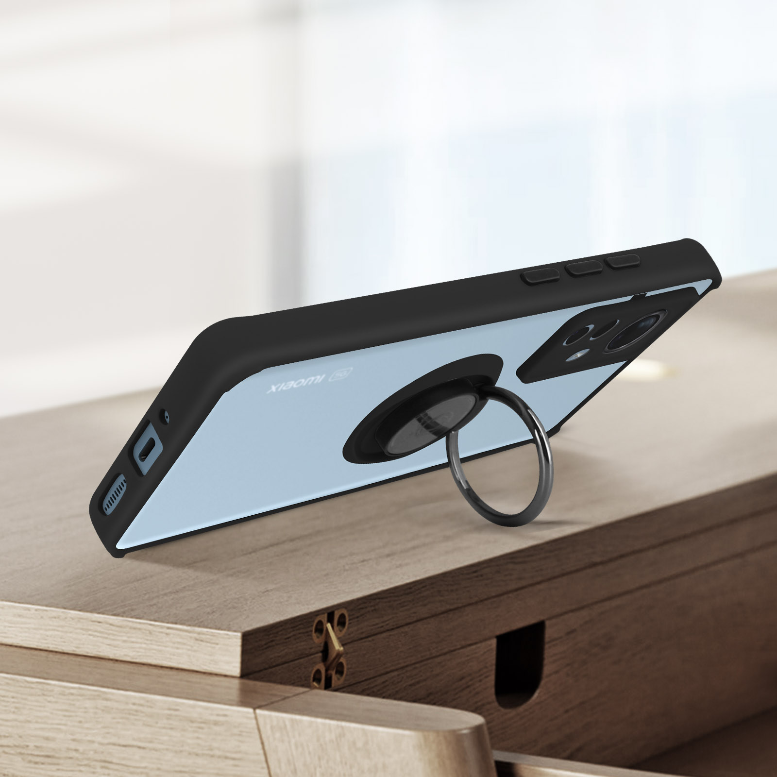 Telefono con anello di supporto, appoggiato su una superficie di legno. Custodia nera con retro blu. Sfondo sfocato.