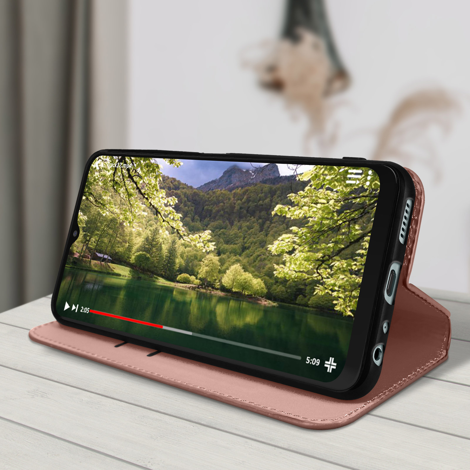 Telefono che mostra un video naturalistico, in una custodia rosa, su un tavolo di legno.