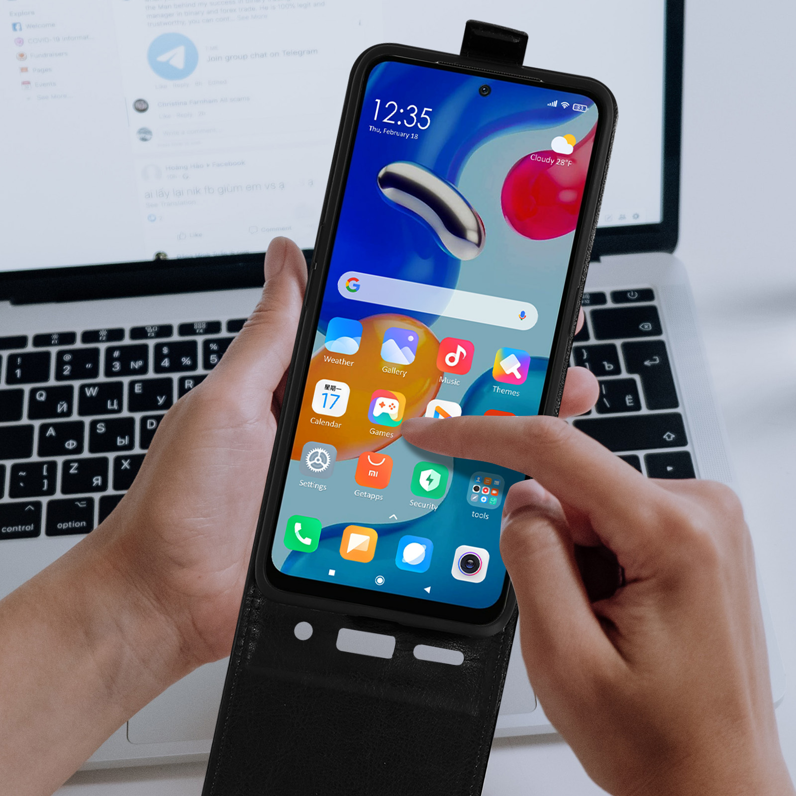 Una persona tiene in mano un telefono che mostra uno schermo di un'app. Un laptop sullo sfondo. Il telefono è in una custodia.