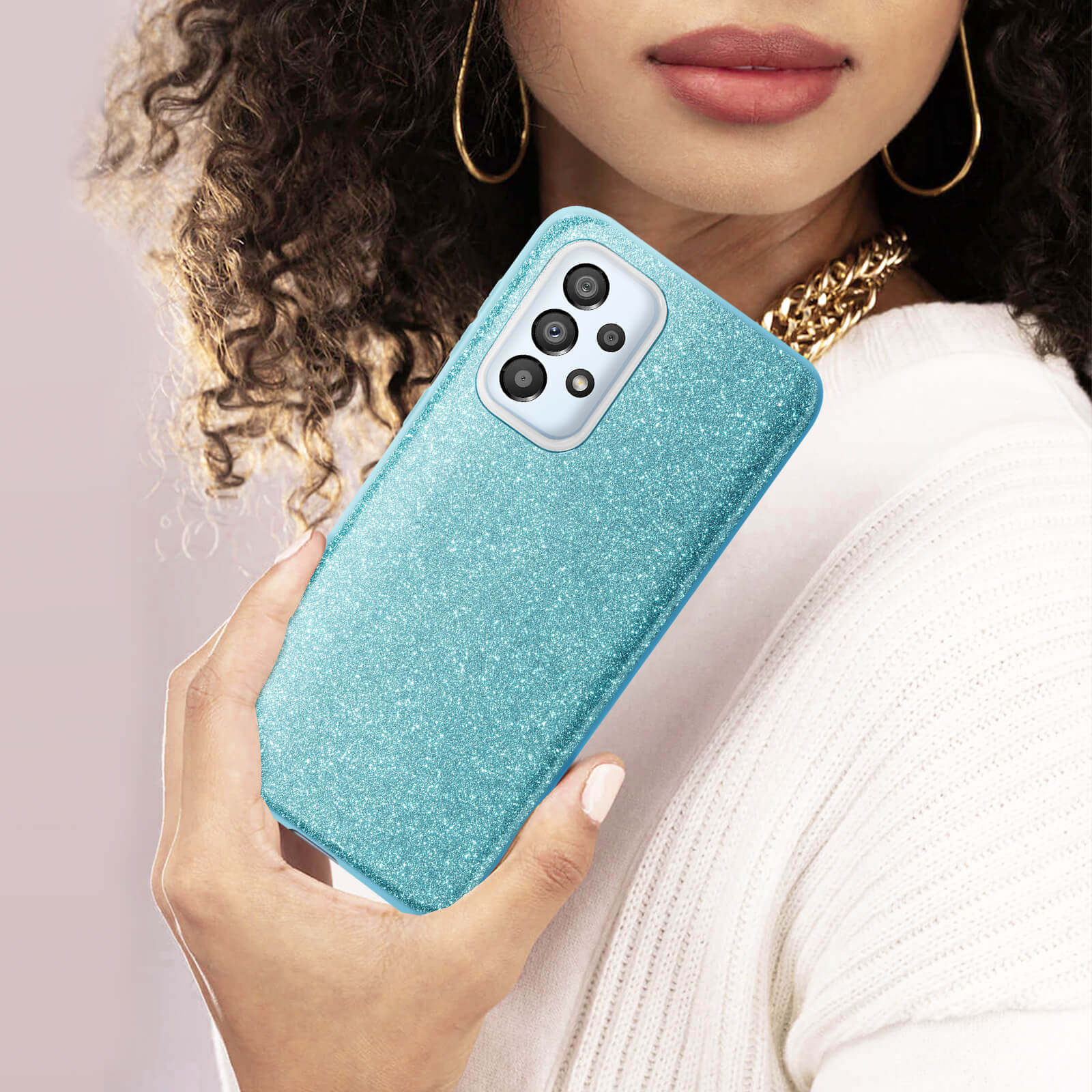 Une femme tenant une coque de téléphone bleu pailleté, collier chaîne doré.