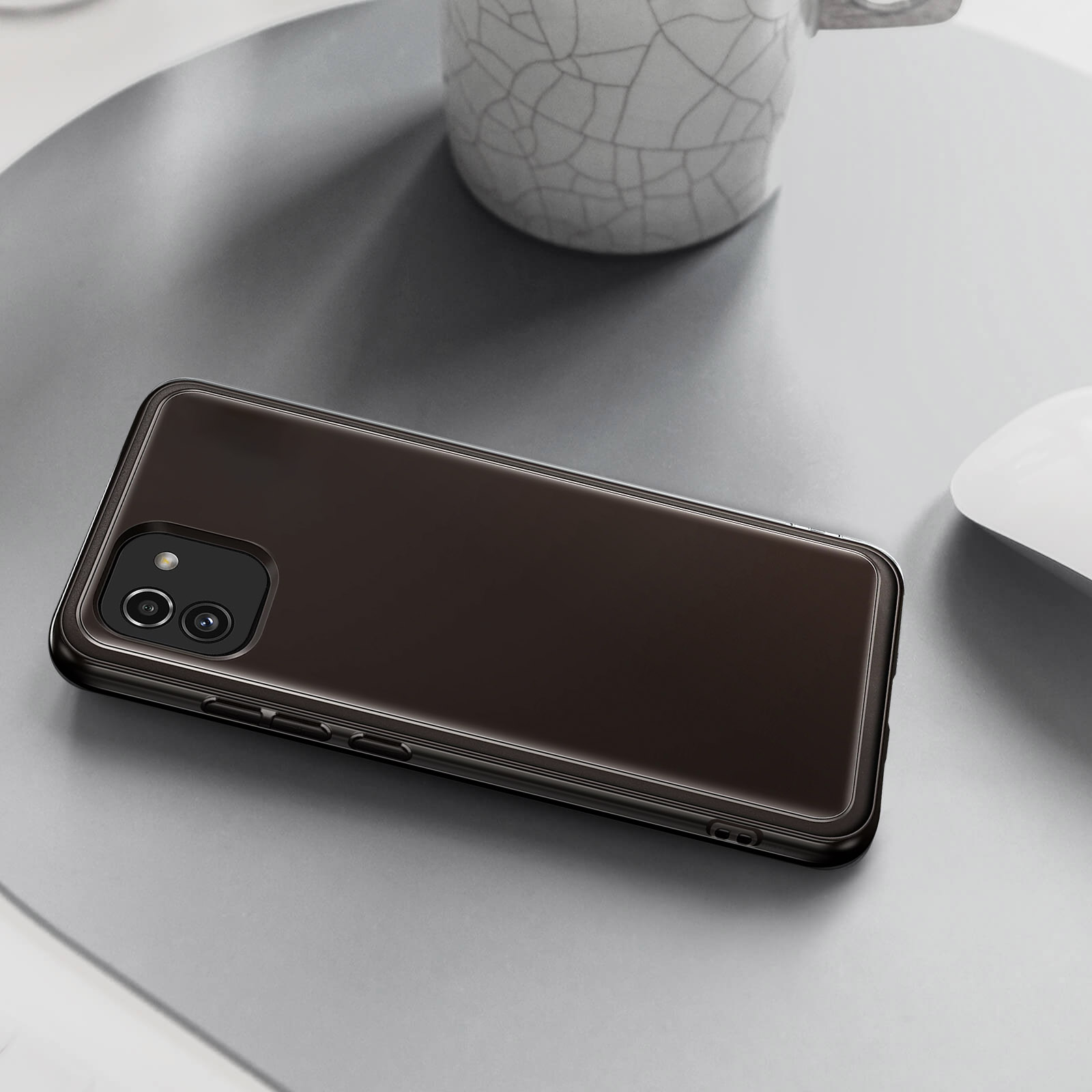 Phone in brown case on gray surface. White mug and mouse are in the background.