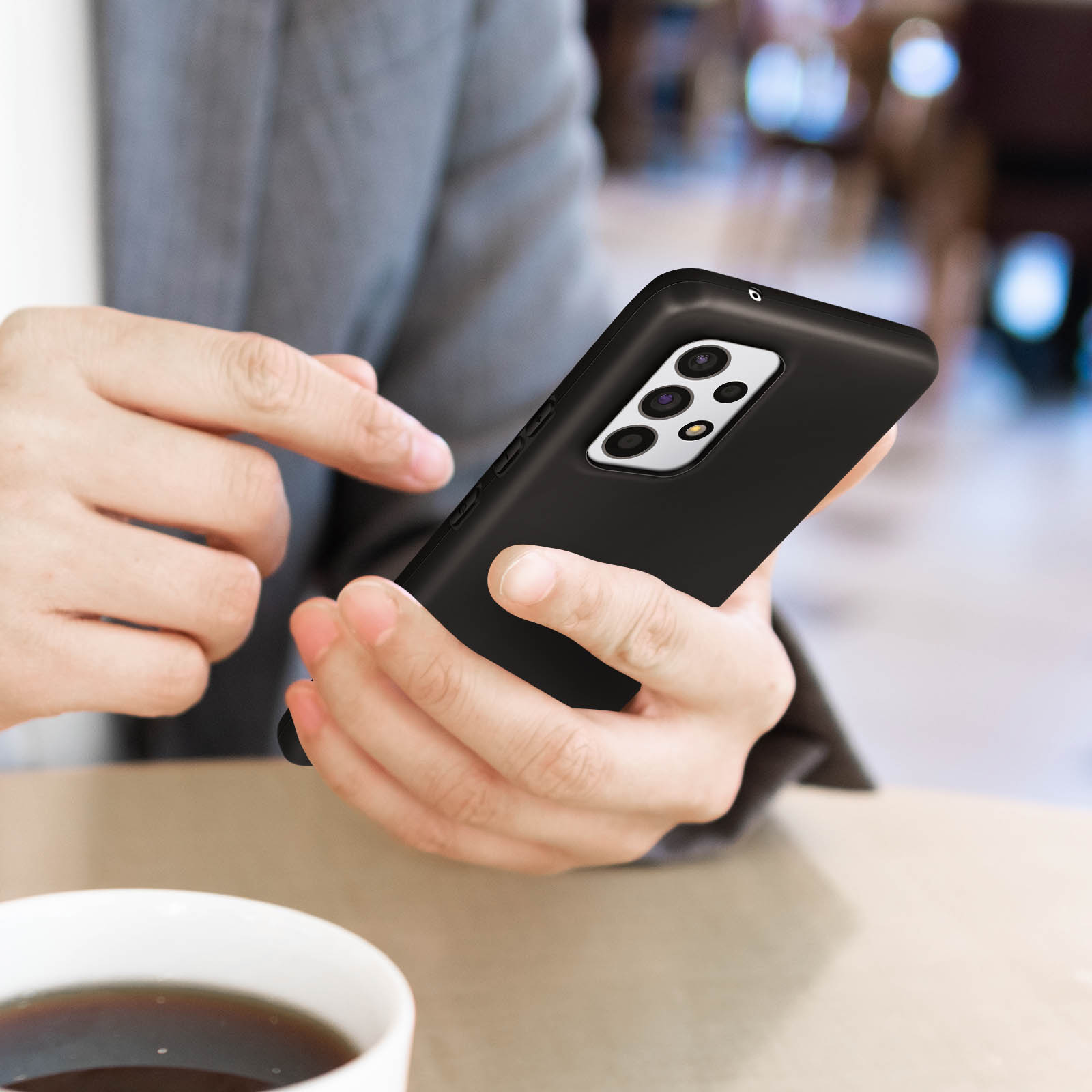 Een persoon houdt een zwarte telefoon in de hand, rustend op een tafel, een kopje koffie staat ernaast.