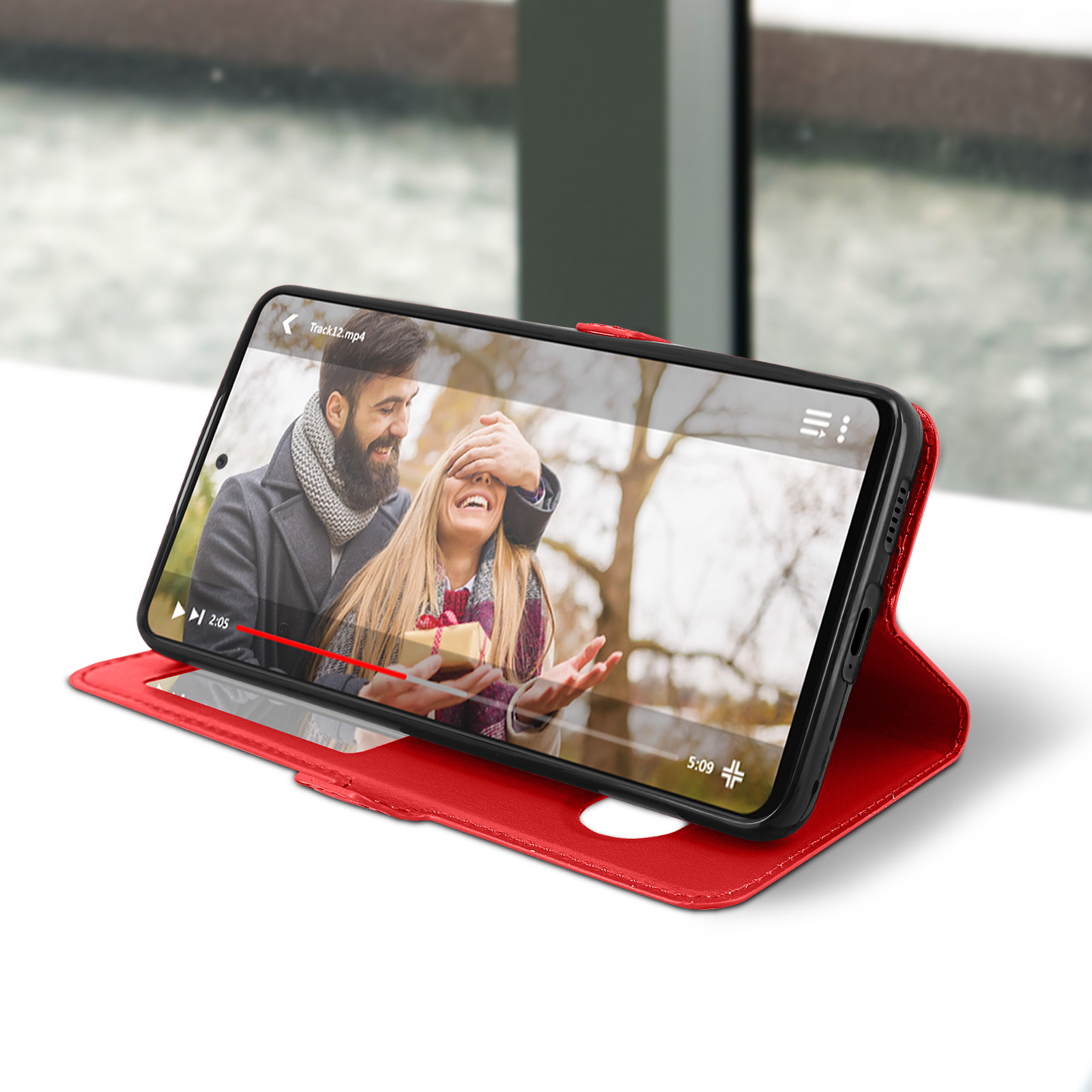 Téléphone dans un étui rouge affiche une vidéo. Un couple à l'écran. L'étui est sur une surface blanche.