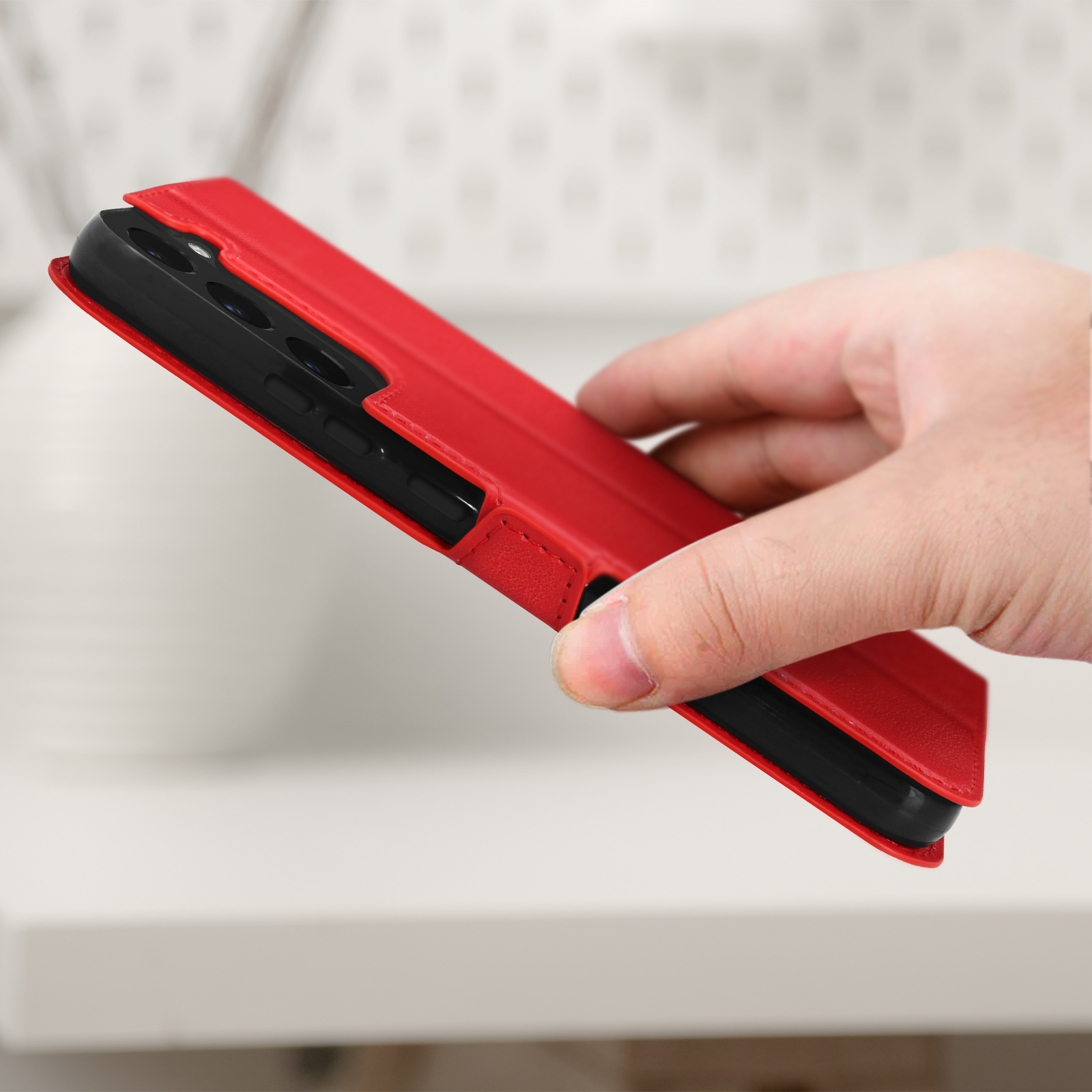 Une main tenant un étui de téléphone rouge avec un téléphone noir à l'intérieur. L'étui est ouvert.