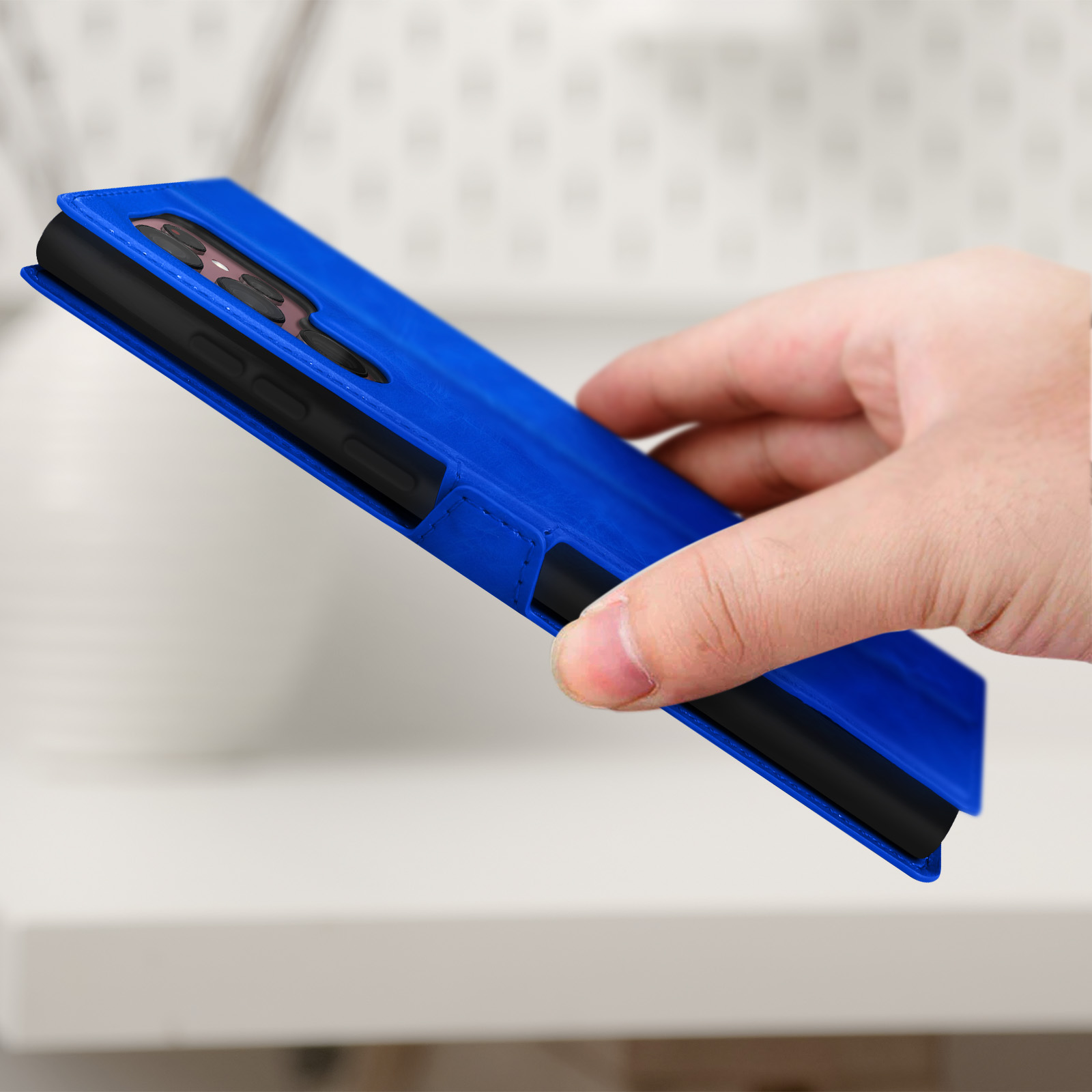 Coque de téléphone bleue pliée ouverte. L'intérieur est noir. Une main la tient.