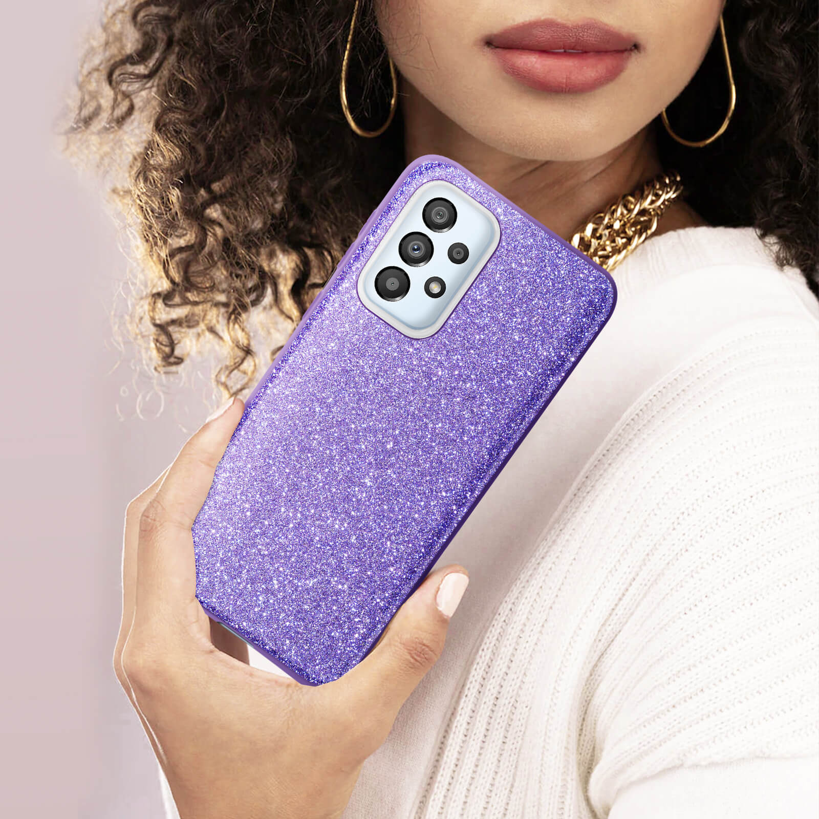 Een vrouw houdt een paarse glitter telefoonhoes vast. Ze draagt een witte trui en een gouden ketting.