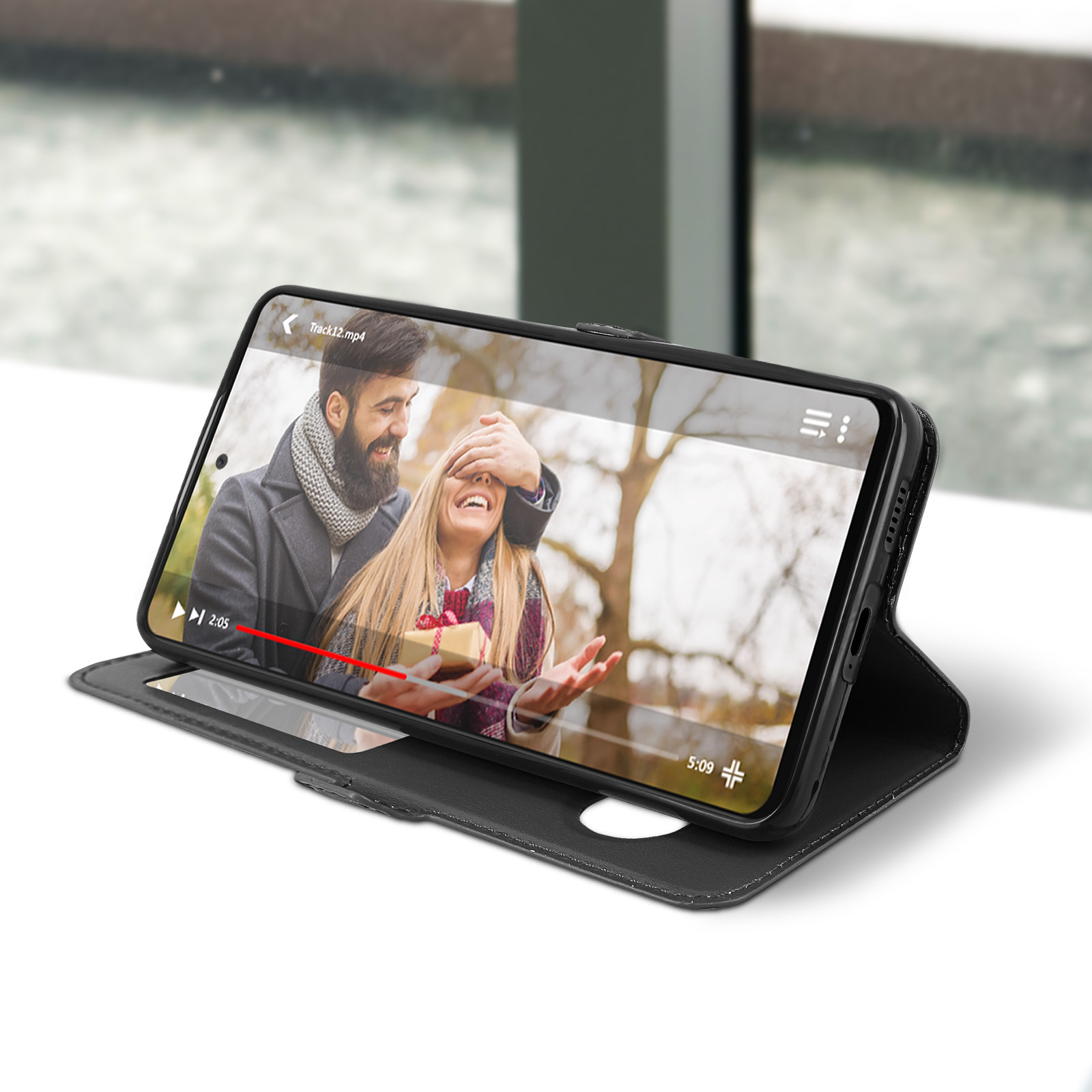 Telefoon in zwarte hoes speelt een video af. Een stel staat op het scherm. De hoes ligt op een oppervlak.