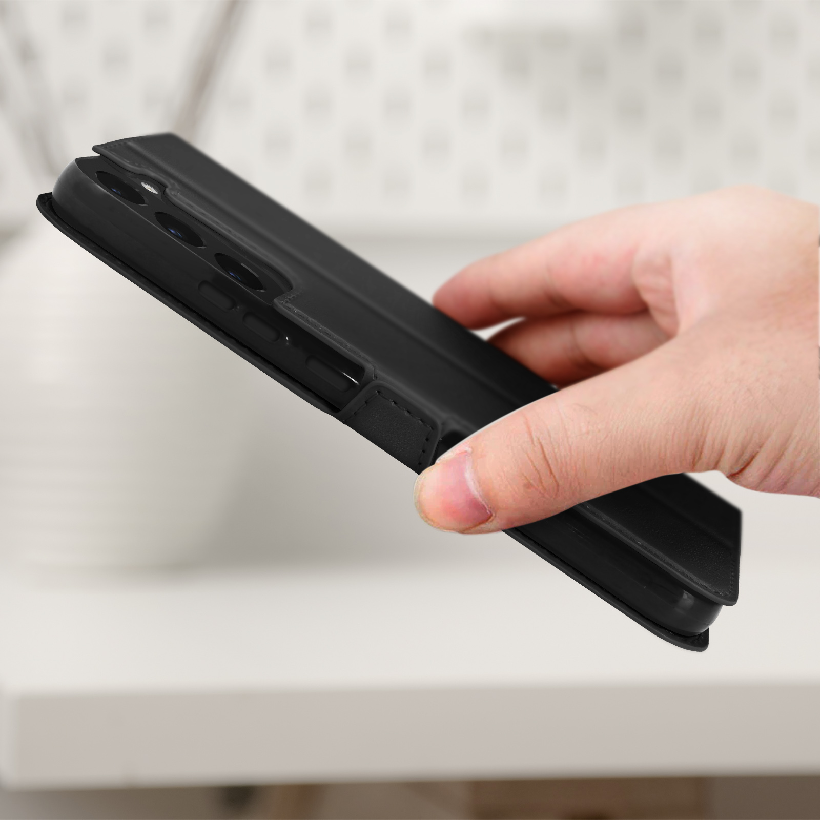 Zwarte telefoonhoes, open, met een telefoon erin. Witte achtergrond, hand houdt de hoes vast.