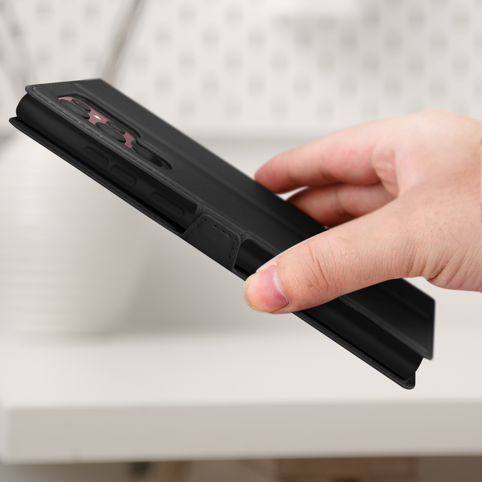 Main tenant une coque de téléphone noire, fermée, sur une surface. Pour la protection du téléphone.