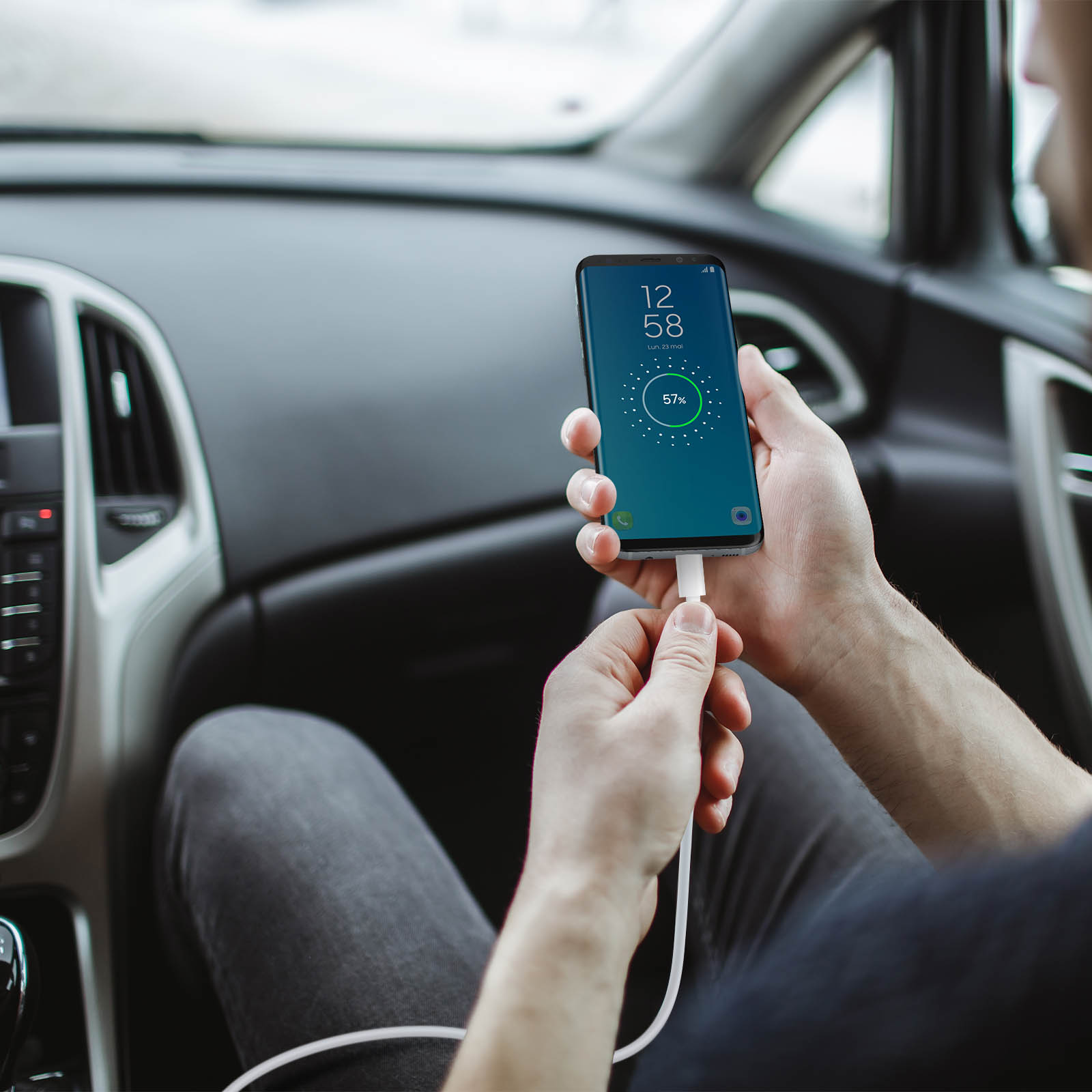 Una persona in auto carica un telefono. Il telefono mostra il 57% di carica. L'interno dell'auto è sullo sfondo.