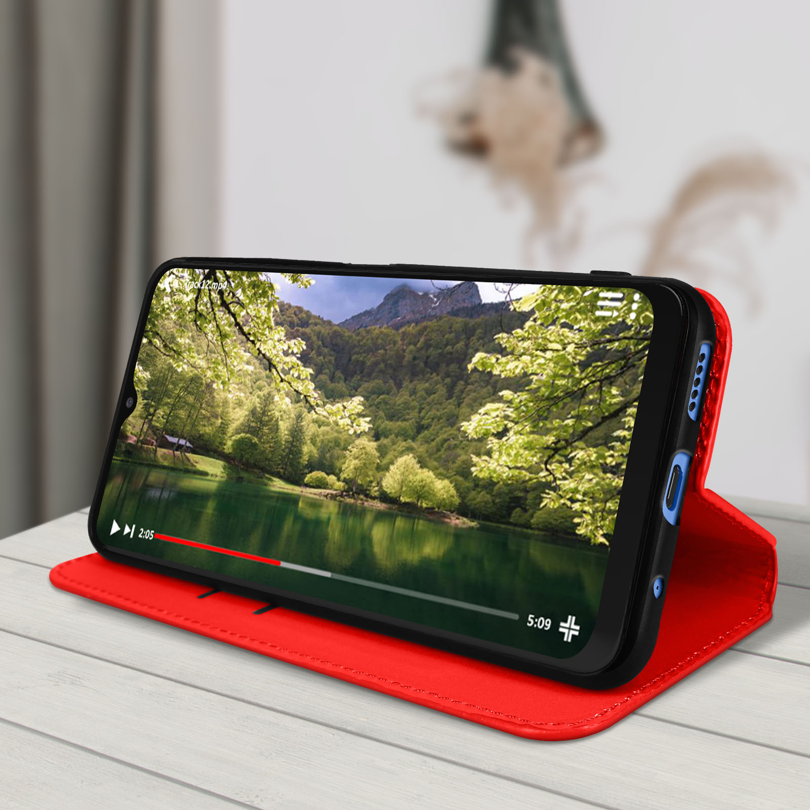 Téléphone affichant une vidéo avec vue sur le lac sur une table en bois. Couverture rouge.