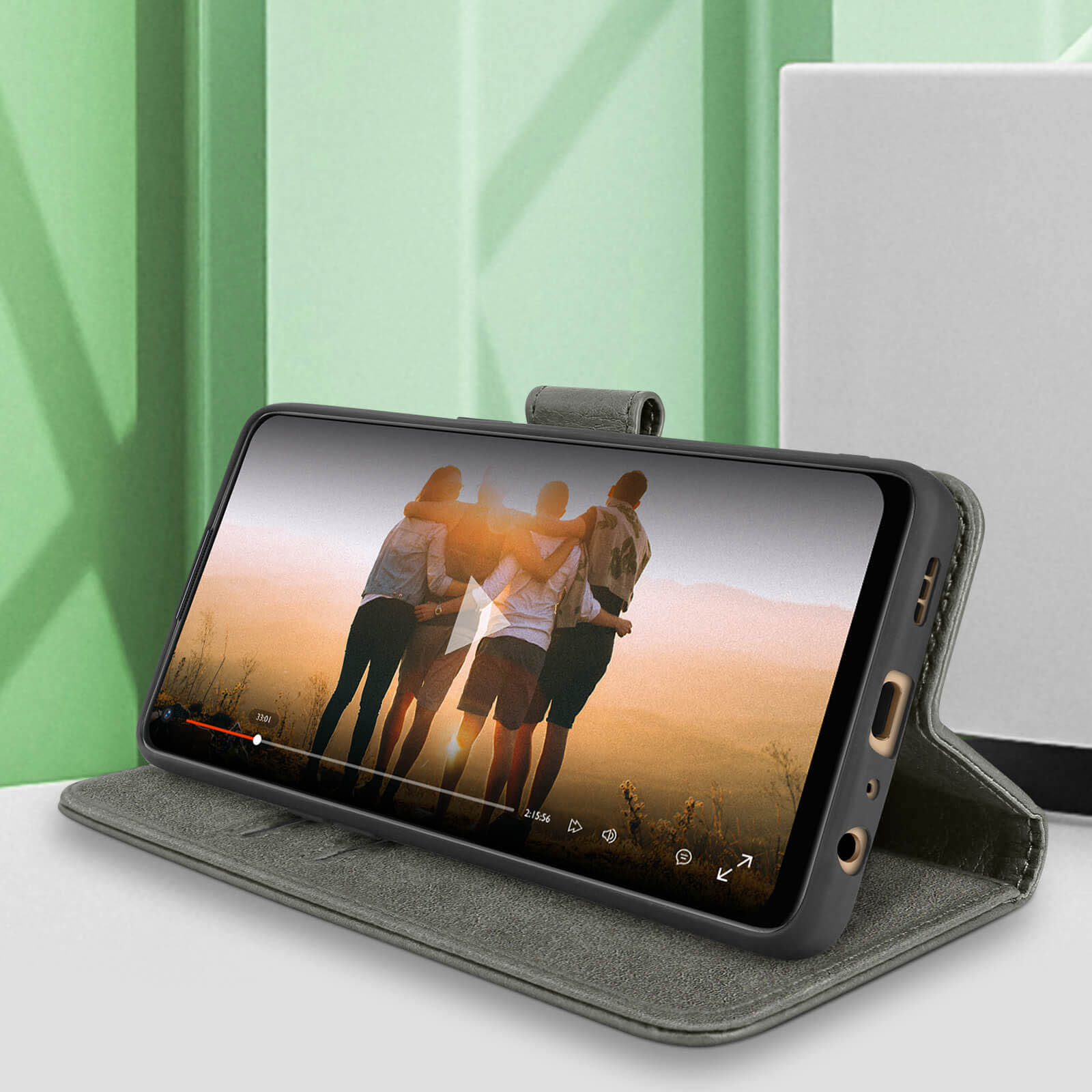 Le téléphone diffuse une vidéo de personnes. Il est dans un étui gris sur une table.