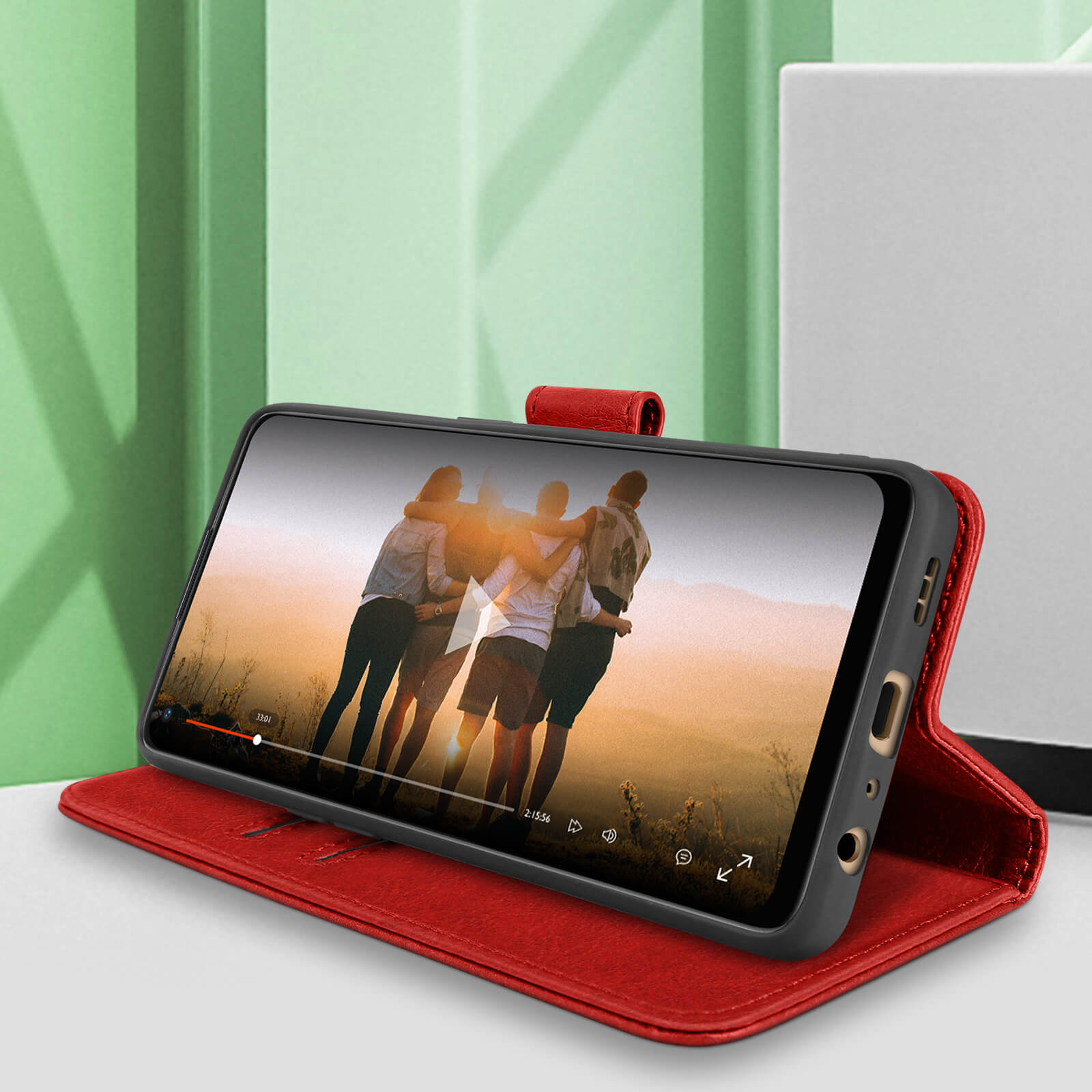 Un étui de téléphone rouge avec un téléphone affichant une vidéo, sur une table. Une personne regarde la vidéo.