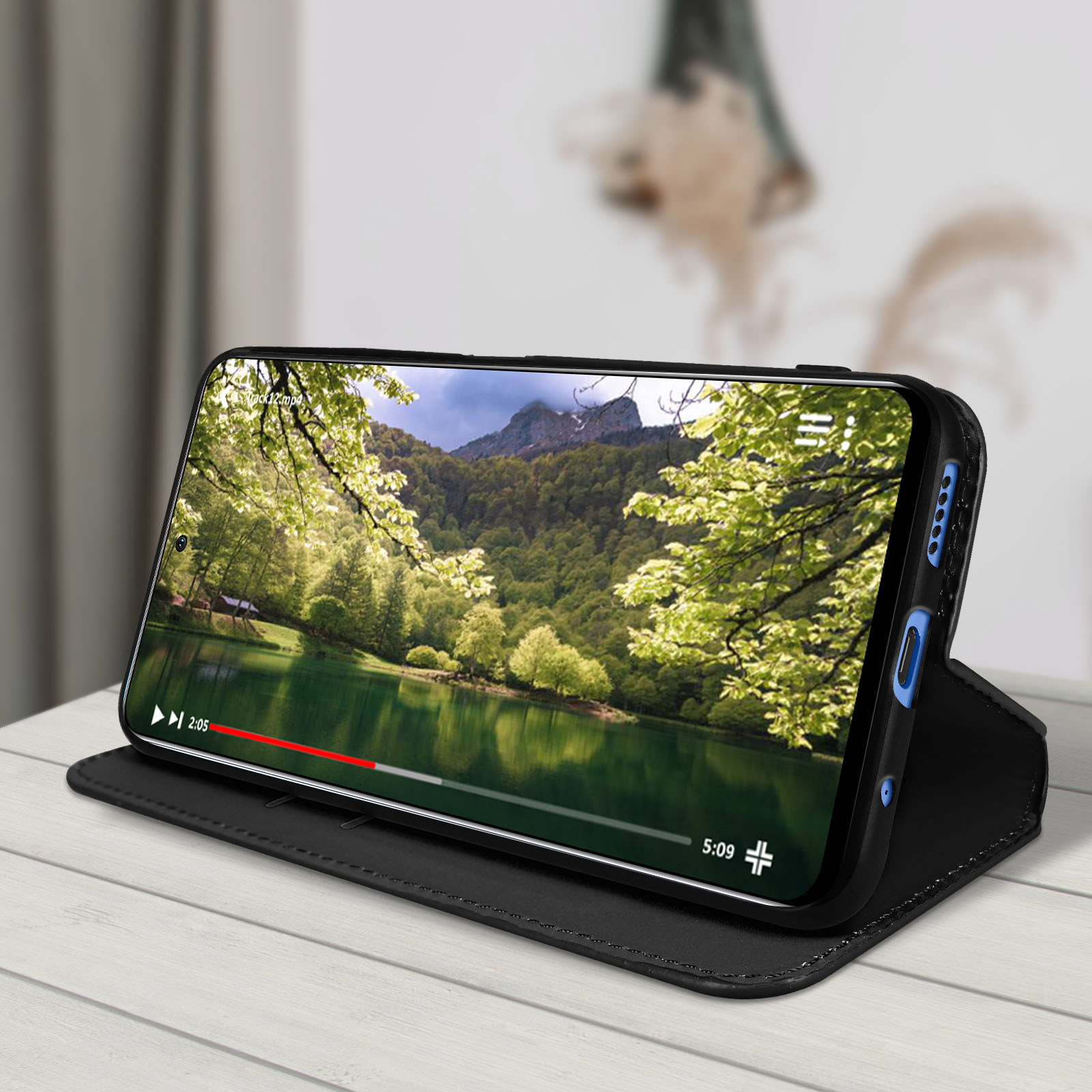 Téléphone dans un étui folio noir. Montre une vidéo d'un lac et des montagnes. Étui sur bois.