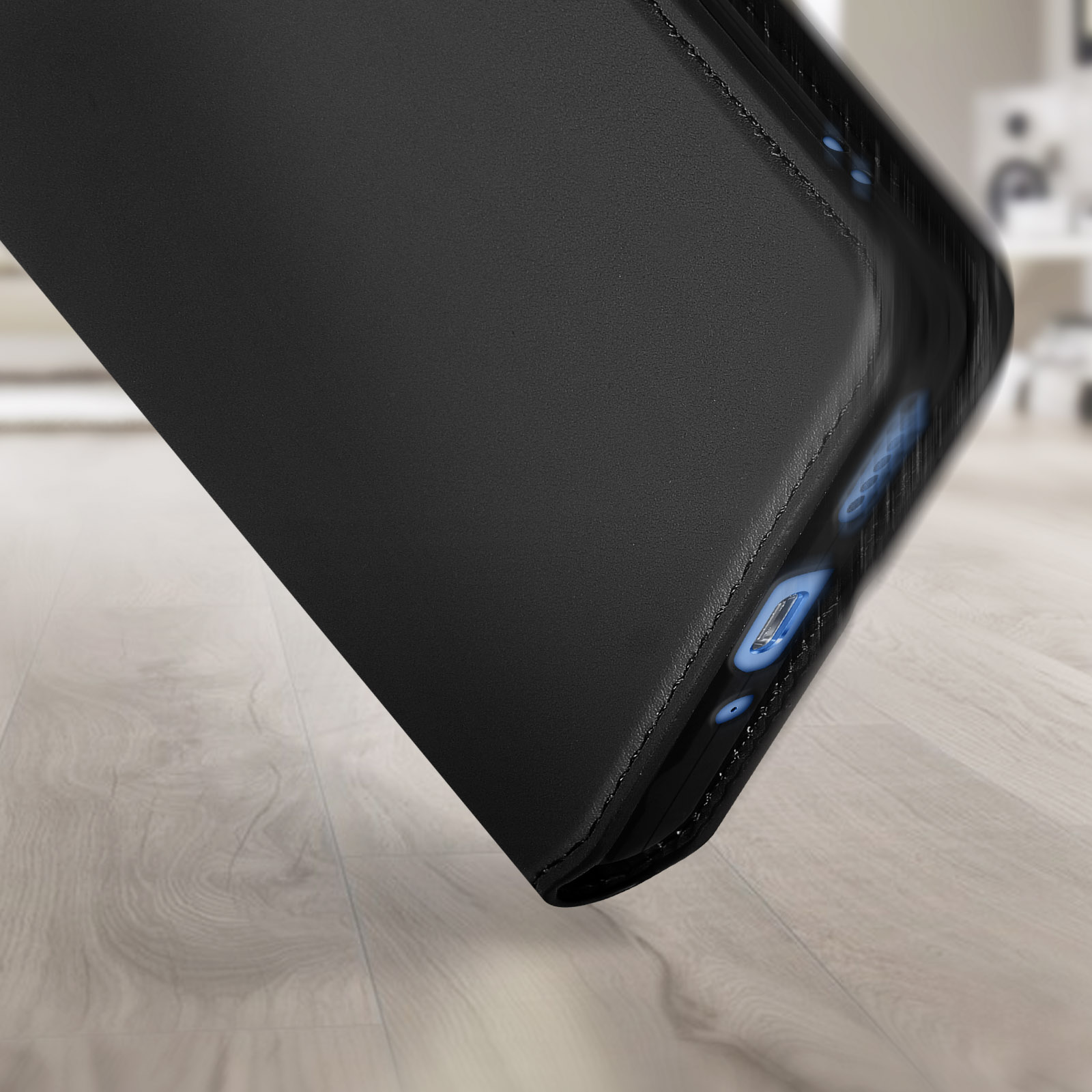 Une coque de téléphone noire est posée sur une surface en bois. Le bord est visible, montrant un port de charge bleu.