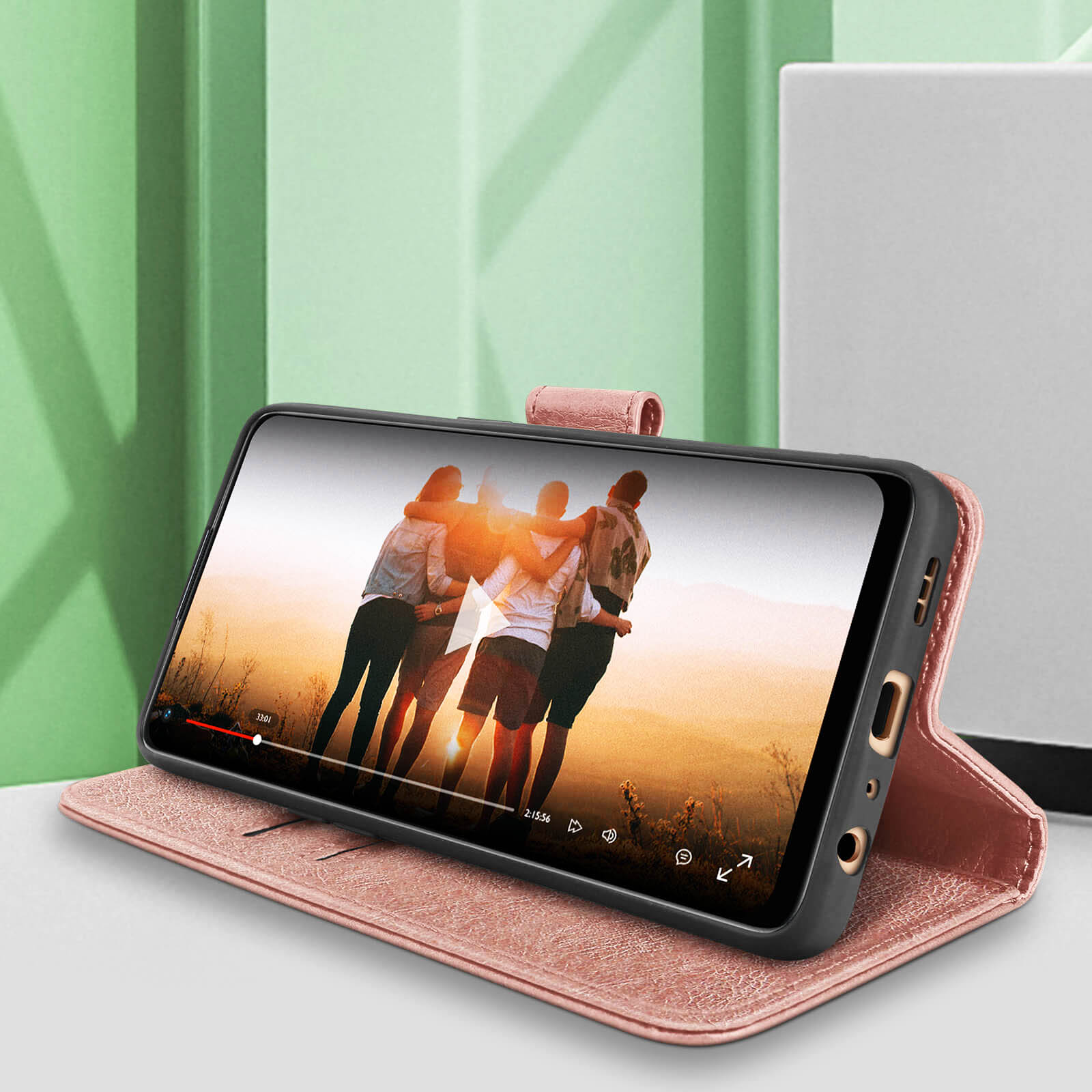 Un téléphone dans un étui rose affiche une vidéo de personnes. Étui ouvert sur une table avec de la verdure.