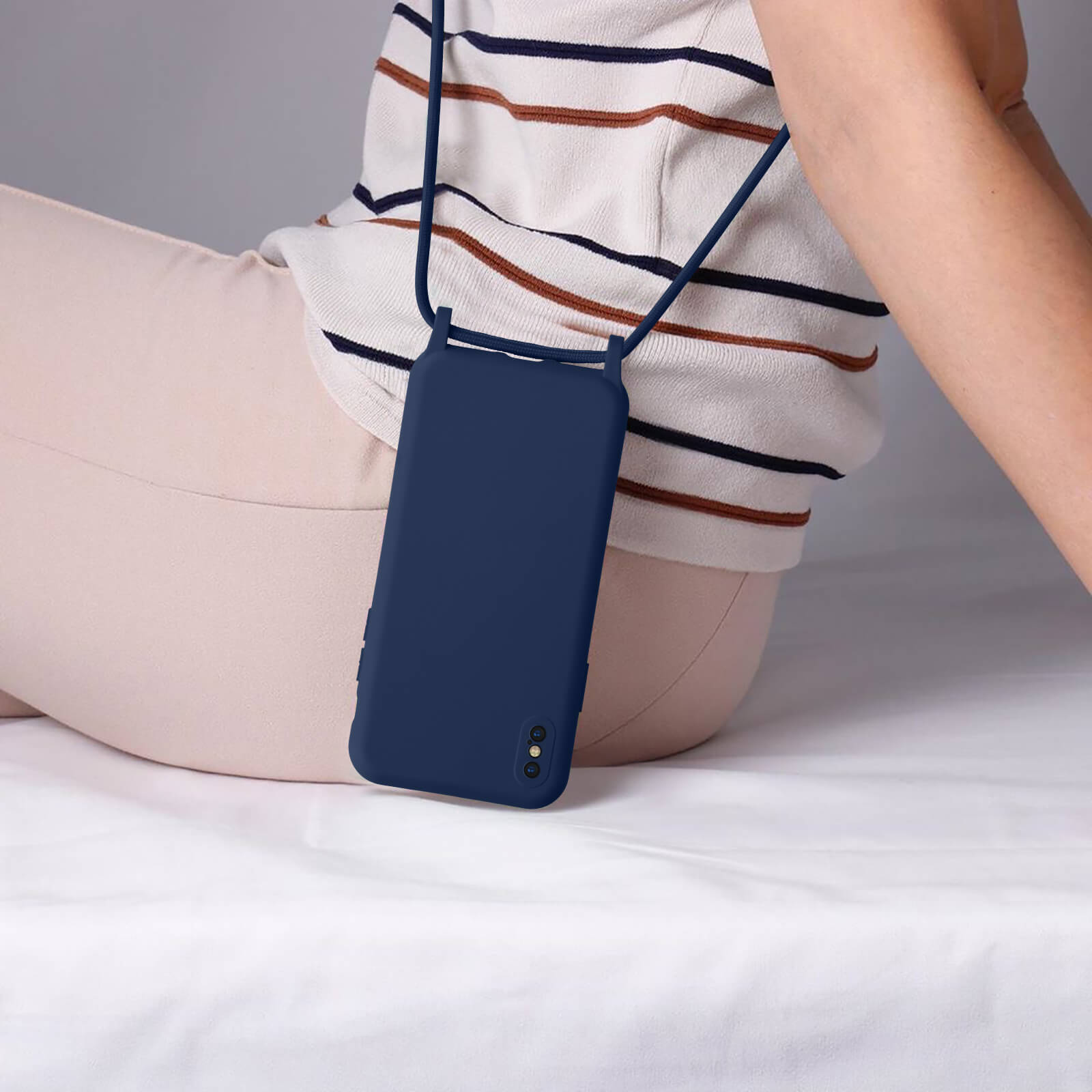 Une personne portant une coque de téléphone bleu marine avec une sangle. Pantalon beige, fond blanc.