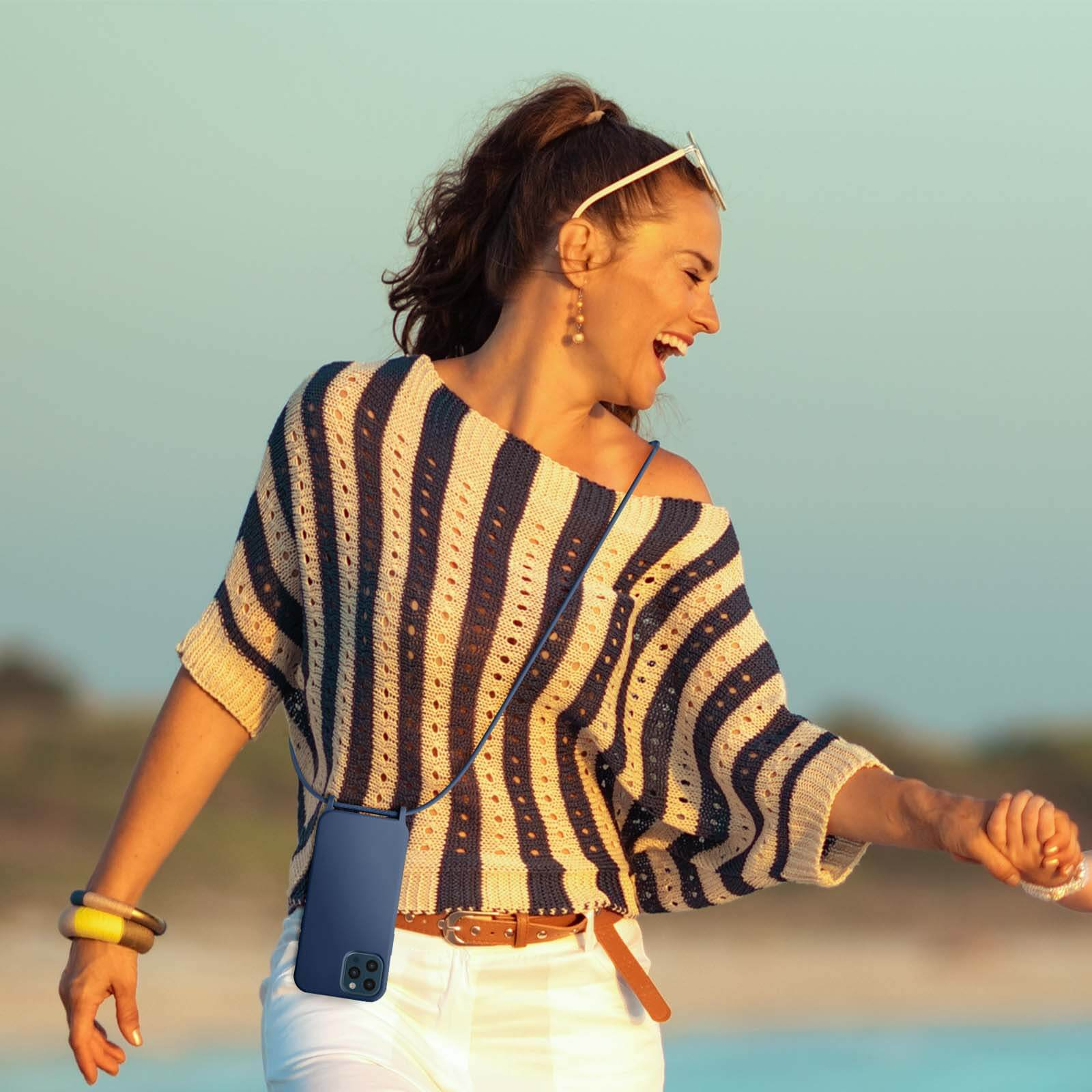 Una donna con una camicia a righe tiene una custodia blu per telefono con un telefono in spiaggia.