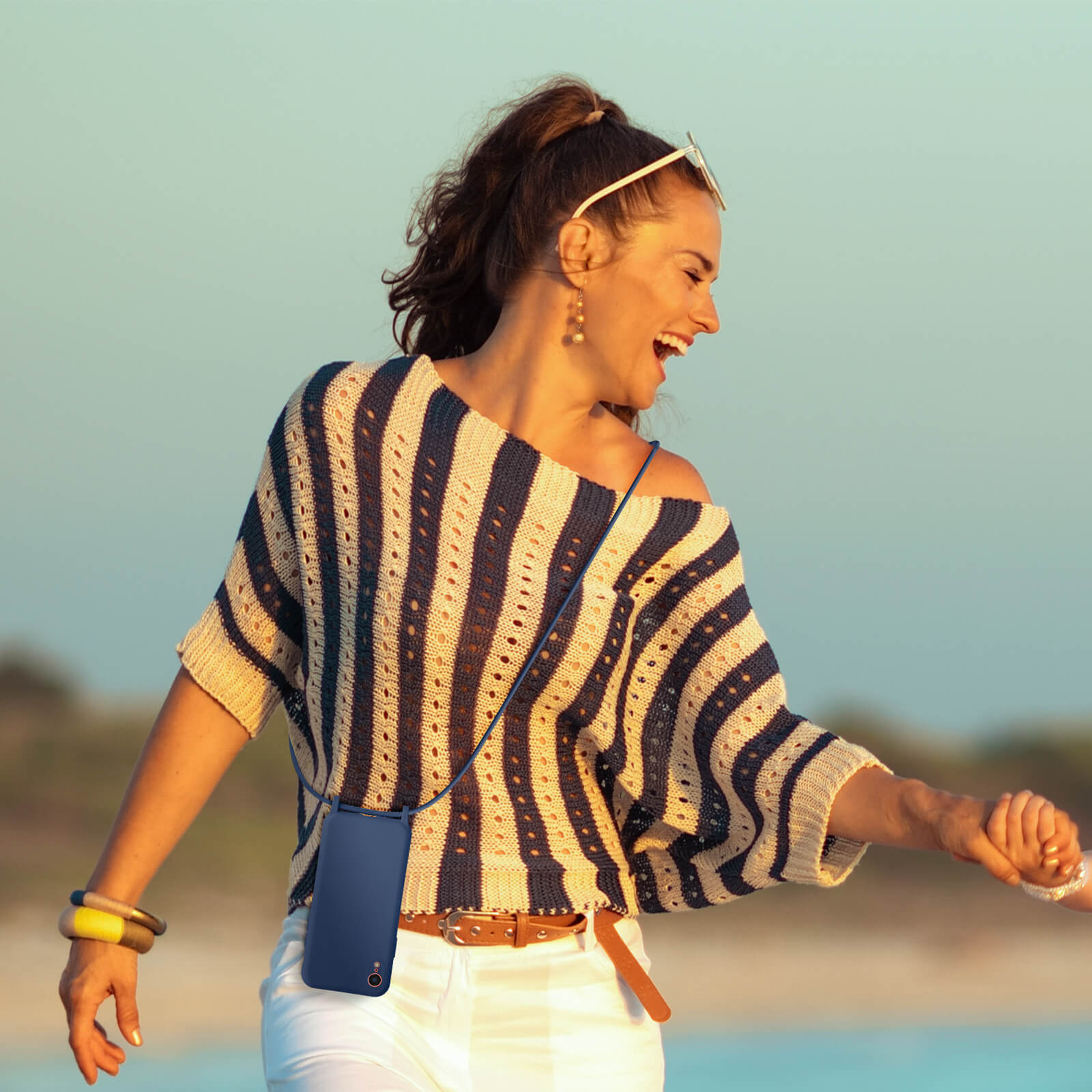 Femme portant un collier de coque de téléphone bleu, souriante et marchant dehors.
