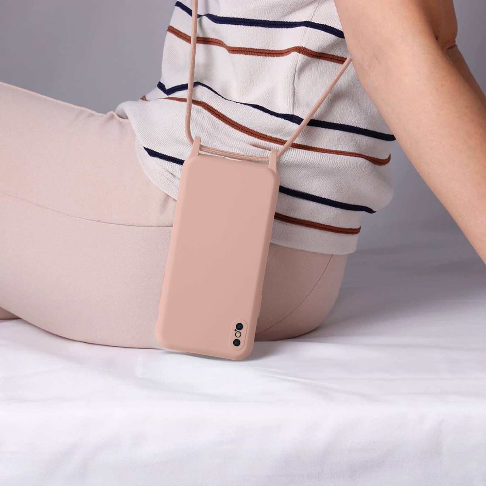 Un téléphone rose avec un cordon autour du cou, suspendu sur une surface blanche.