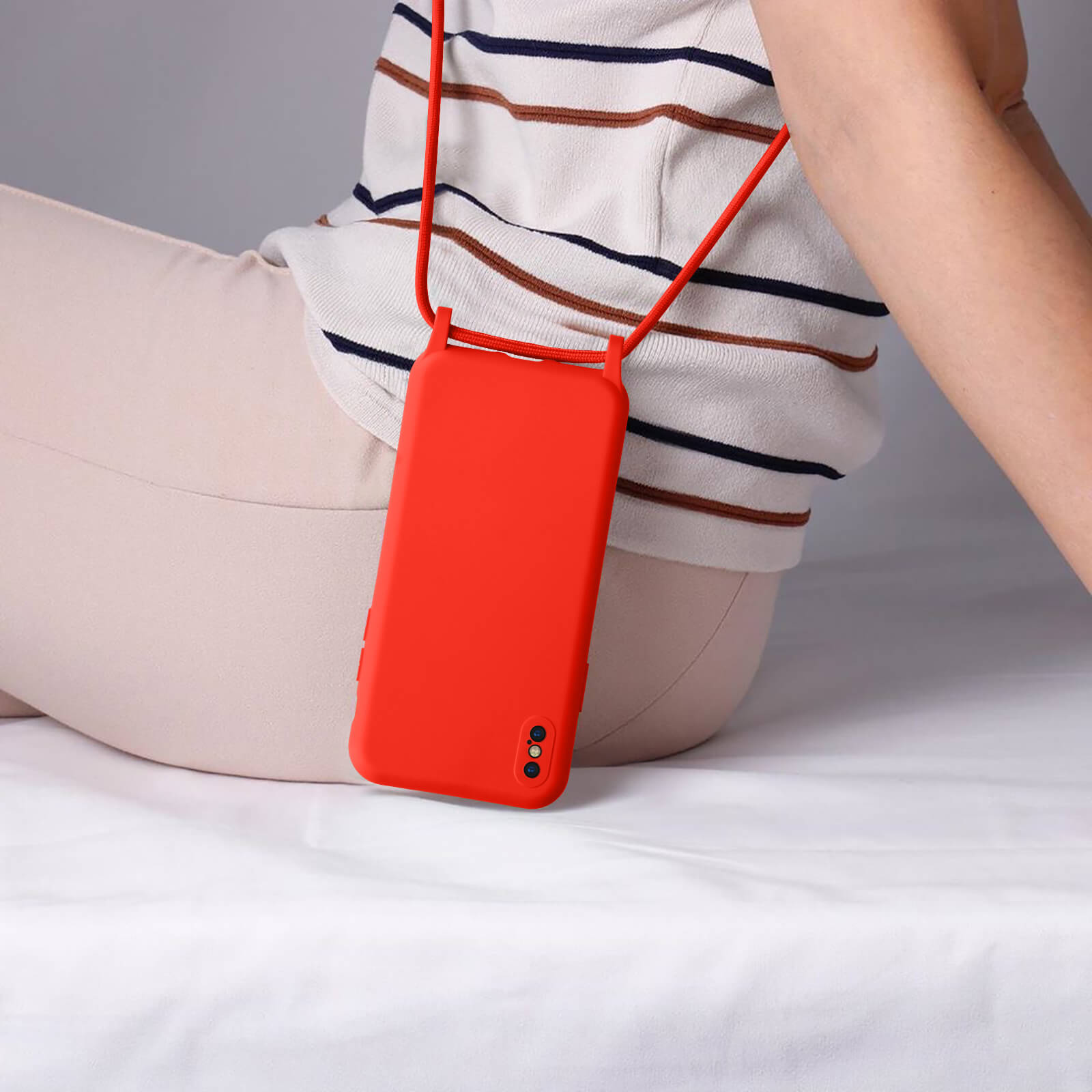 Une personne portant une coque de téléphone orange avec une sangle. Pantalon beige et fond blanc.