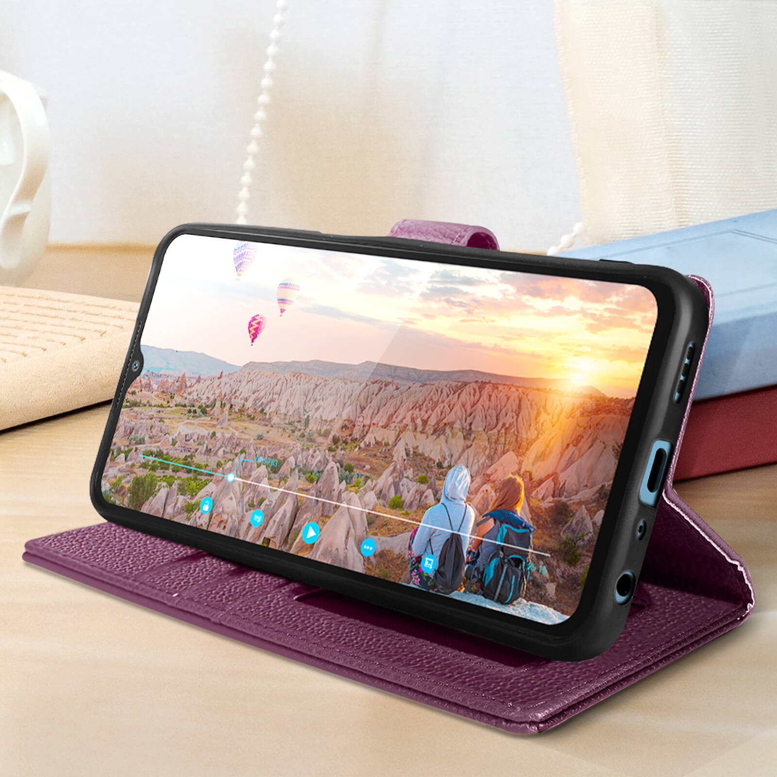 Custodia per telefono viola con telefono che mostra un paesaggio con mongolfiere. Libri sullo sfondo.