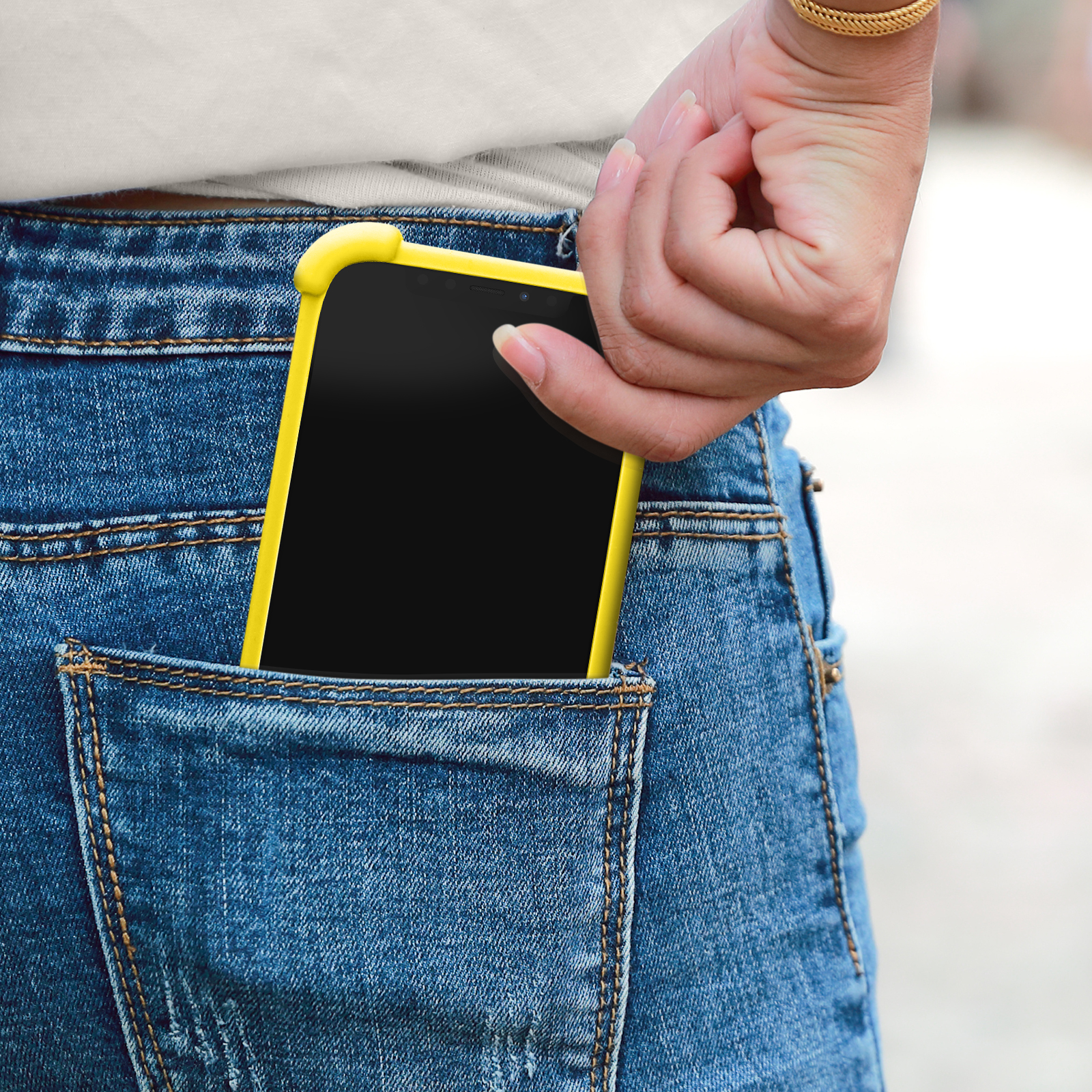 Téléphone dans une poche de jean, coque jaune, main sur la poche.
