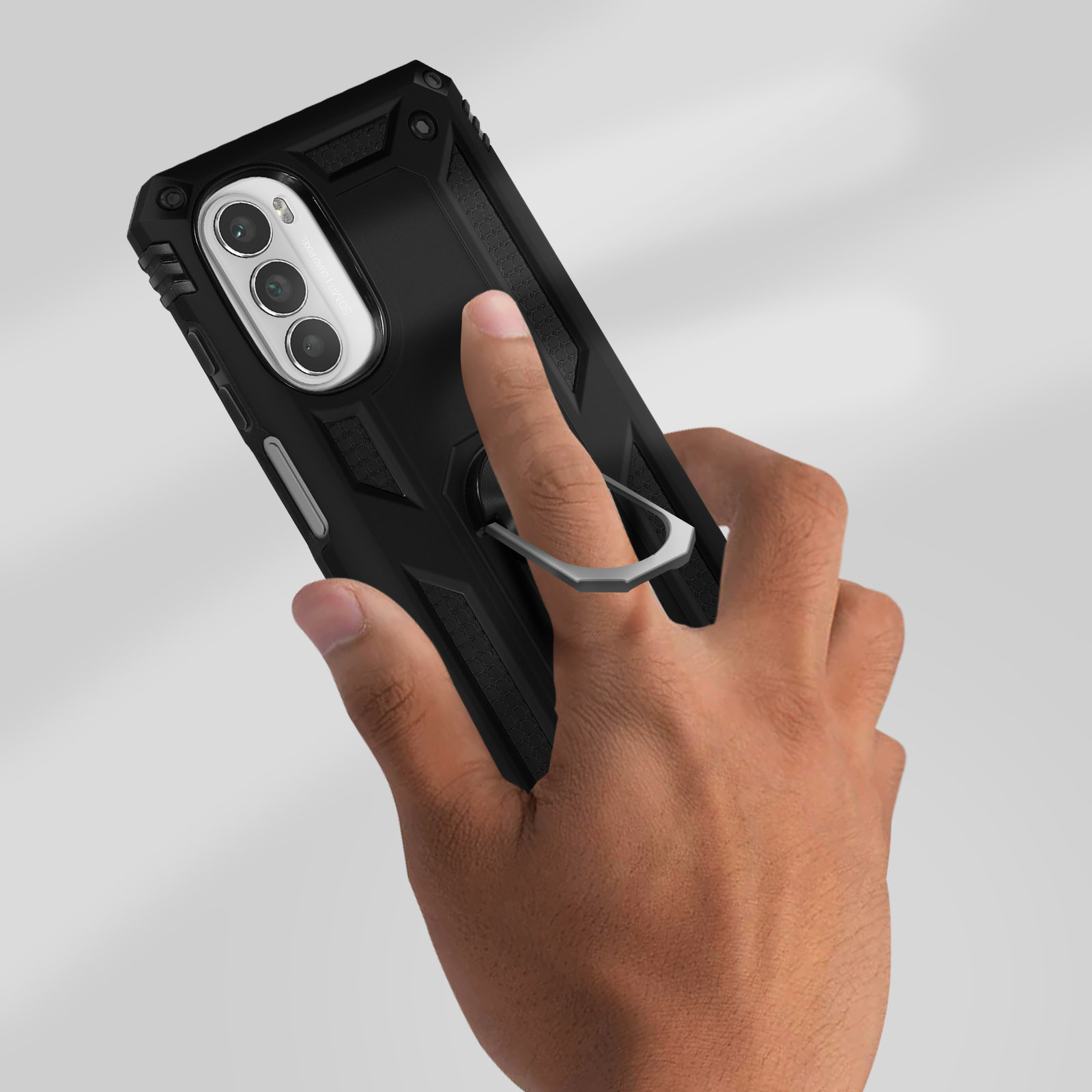 Una mano che tiene una custodia nera con un supporto ad anello argentato. Lo sfondo è una superficie grigio chiaro.