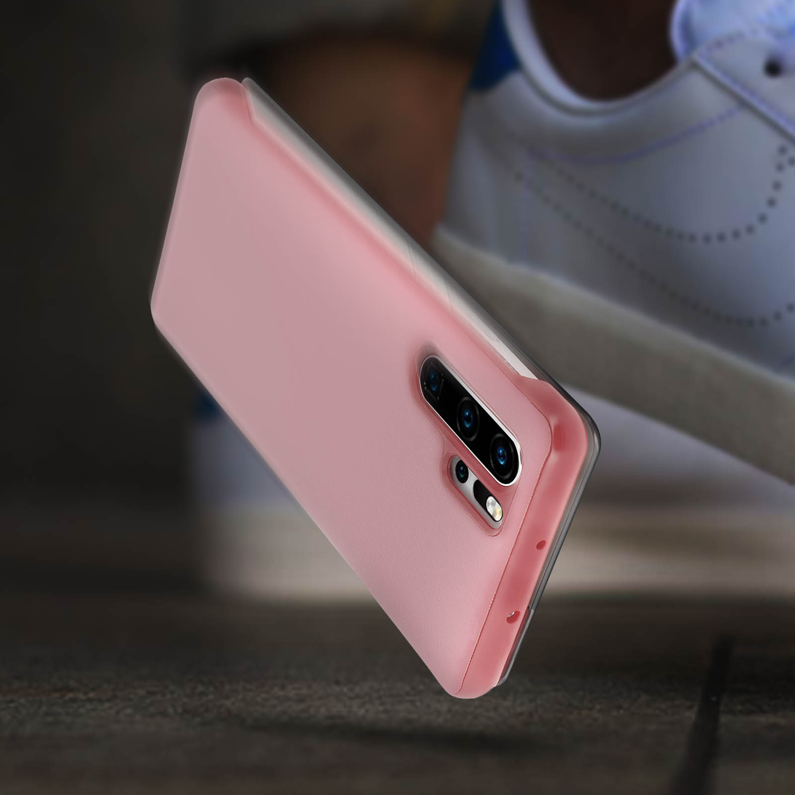 Custodia rosa per telefono in aria. Scarpe da ginnastica e legno sullo sfondo.
