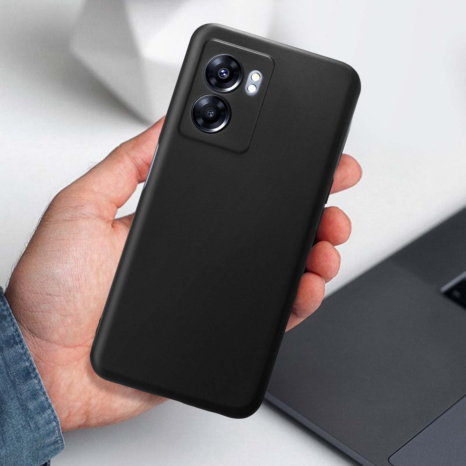 Una mano tiene in mano un telefono. La custodia del telefono è nera. Lo sfondo è un laptop.