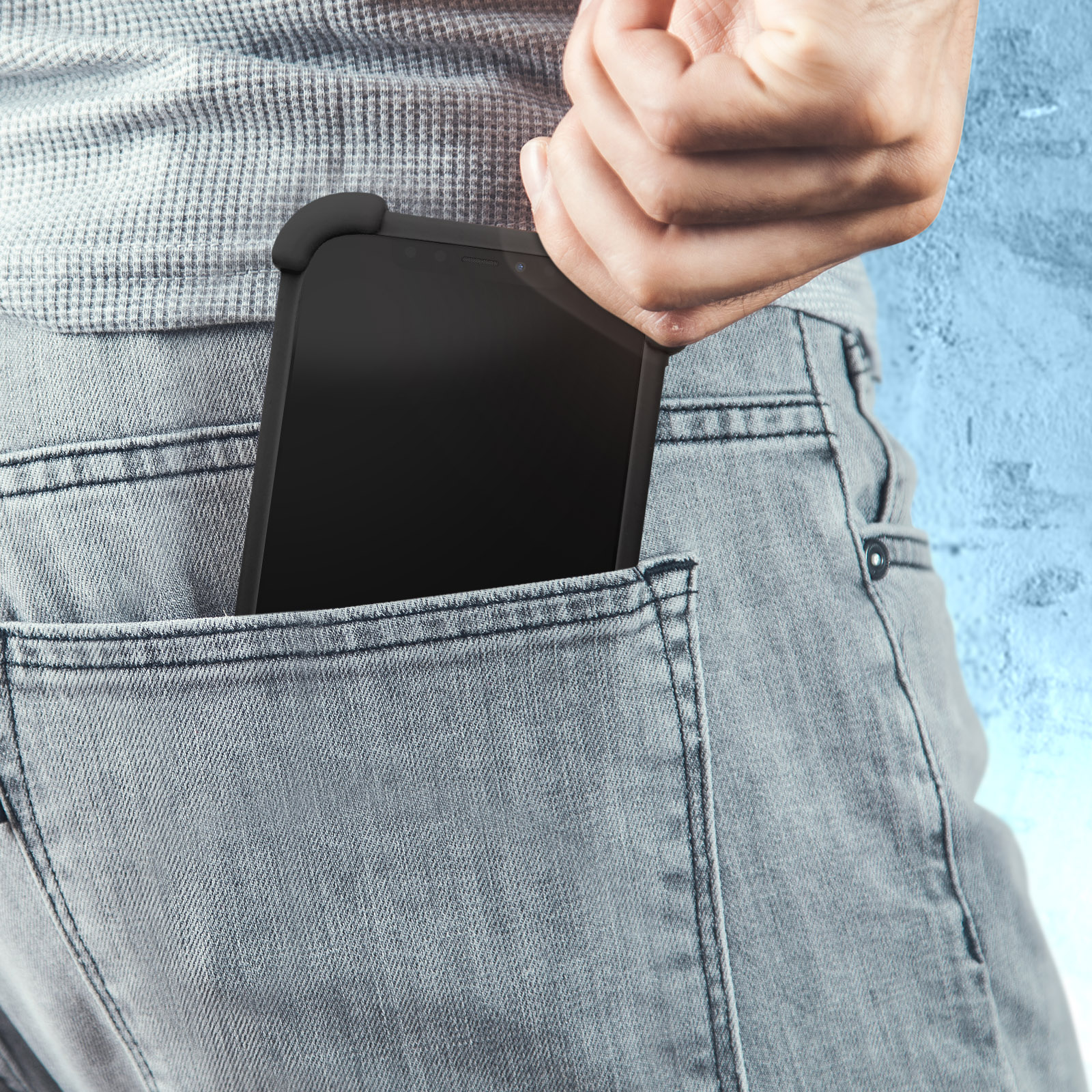 Une personne mettant un téléphone dans sa poche. Le jean est gris.