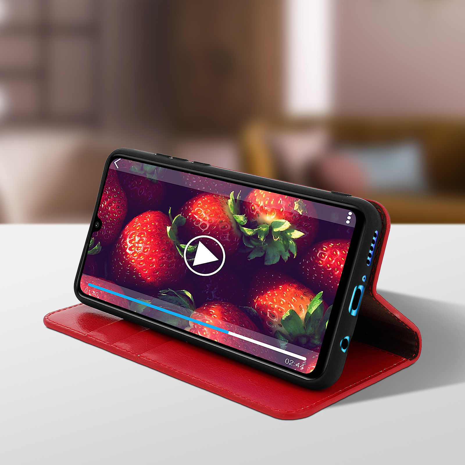 Telefono in custodia rossa, mostra un video di fragole. È su una superficie rossa.