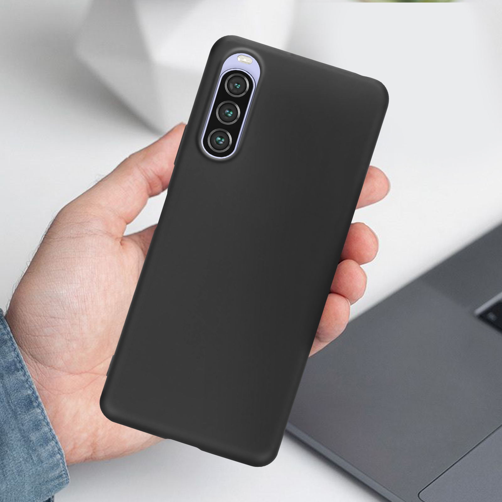 Telefono nero in mano. Tre obiettivi della fotocamera visibili, su una superficie bianca.