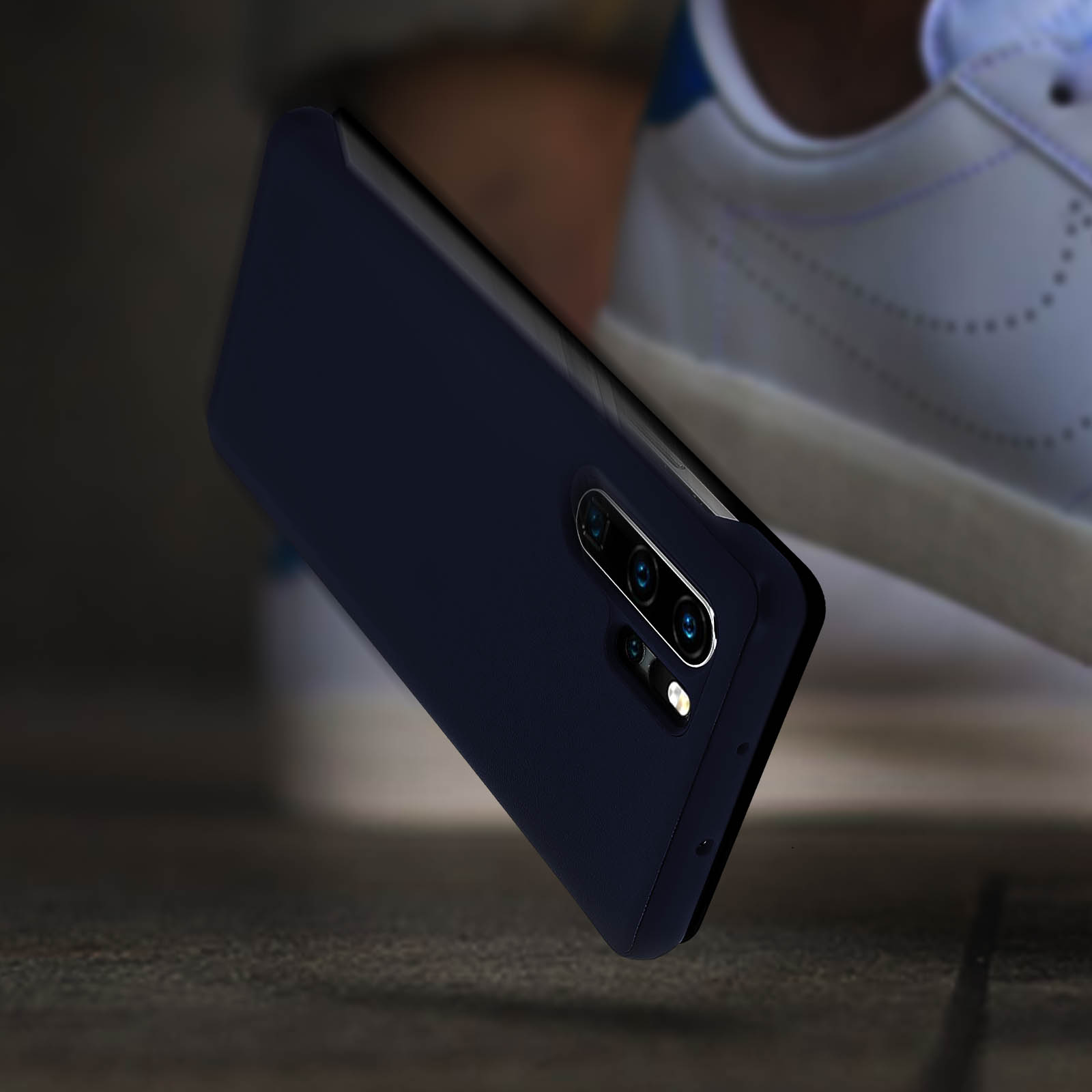 Custodia blu scuro per telefono, vista angolata, mostrata con una scarpa. Sfondo in legno.