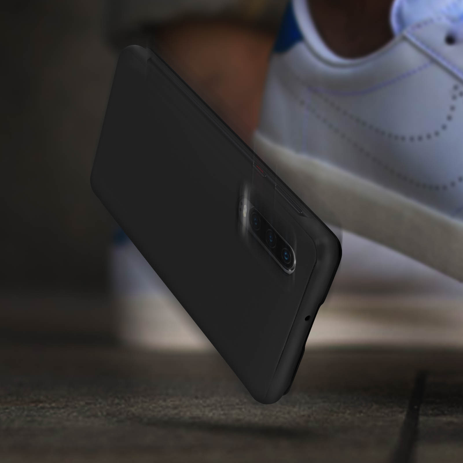 Custodia nera per telefono sul pavimento. Il telefono è inclinato e davanti a una scarpa bianca.