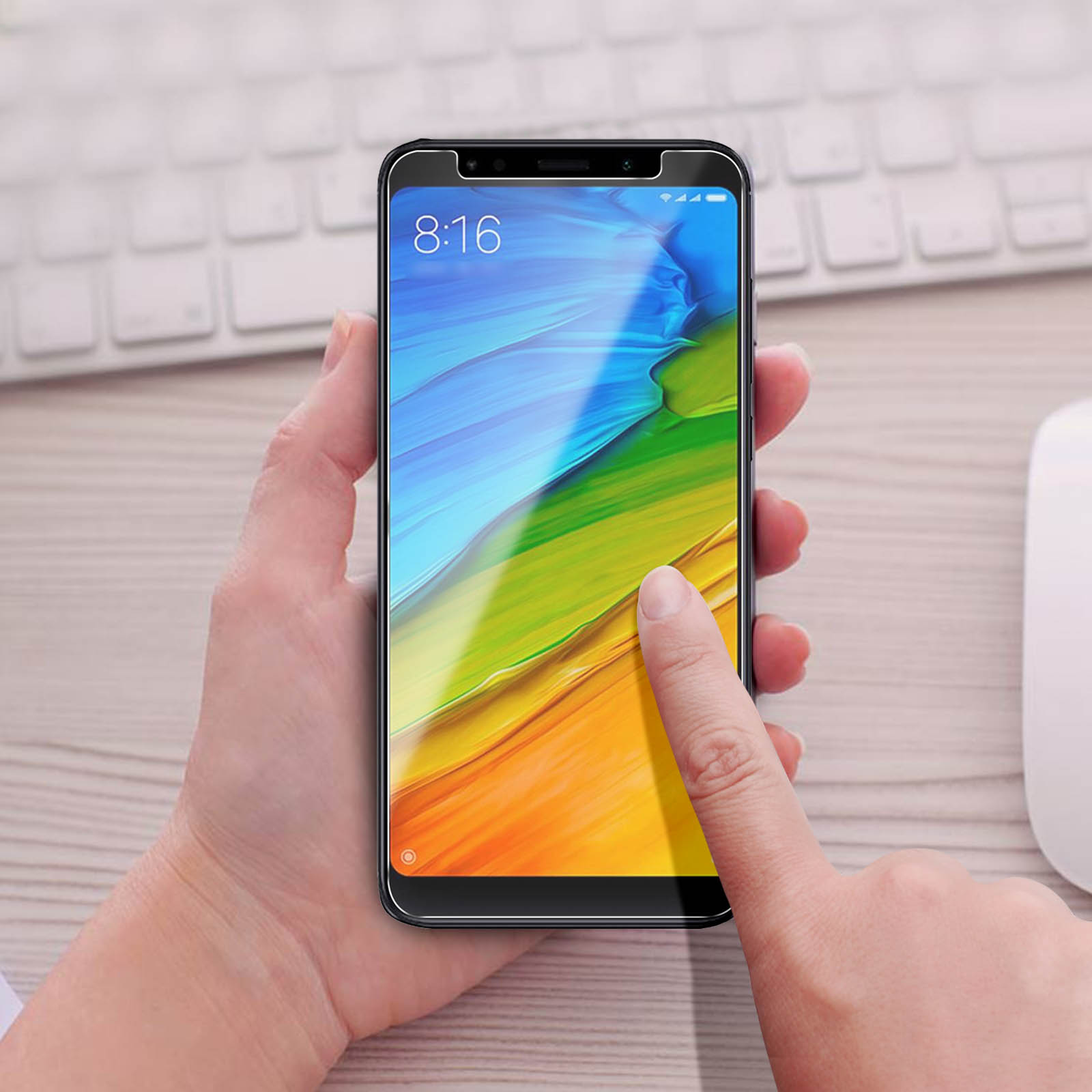 Una mano tocca lo schermo di un telefono con una protezione. Tastiera sullo sfondo.
