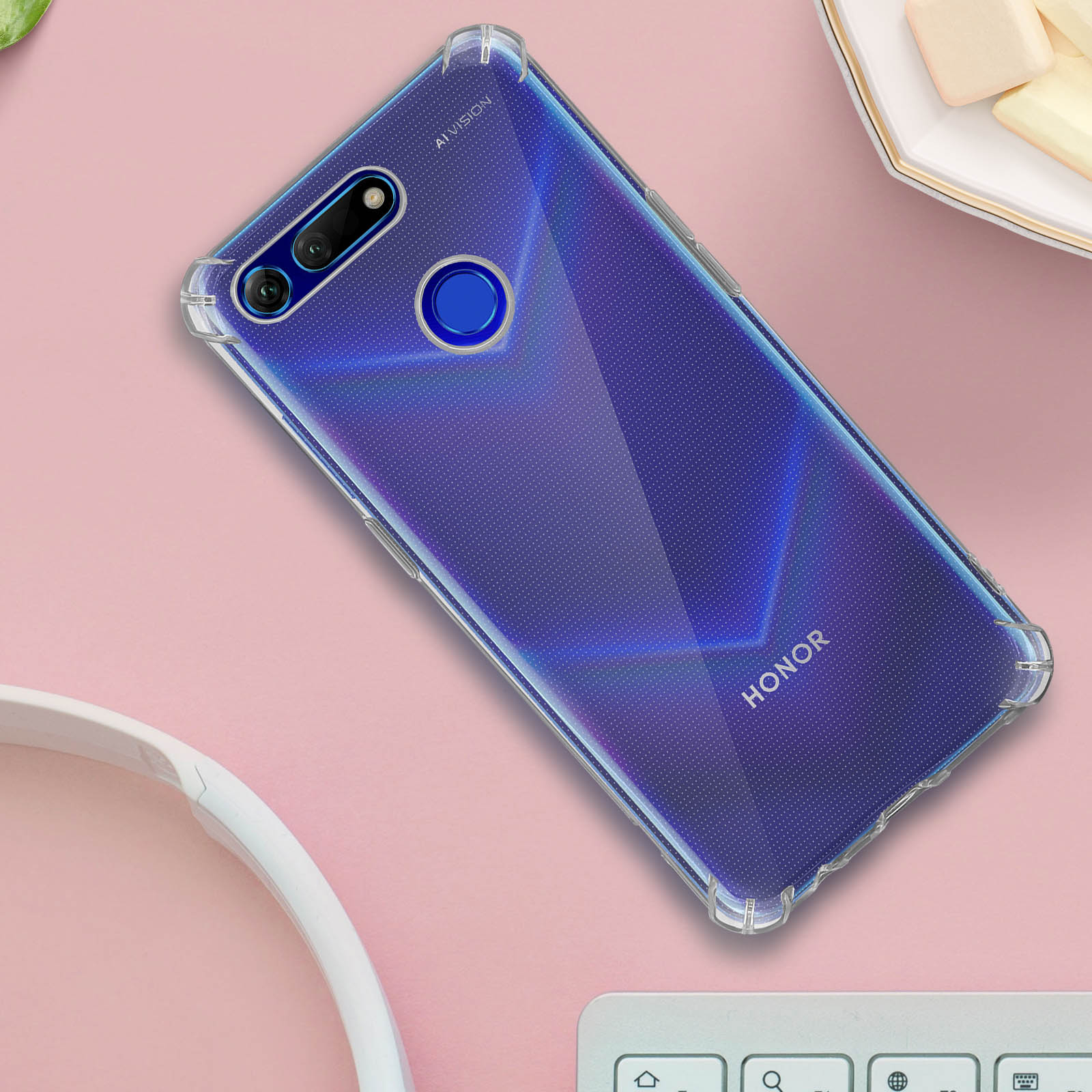 Telefono in una custodia blu trasparente. La custodia è su una superficie rosa. Lo sfondo ha una tastiera e degli snack.